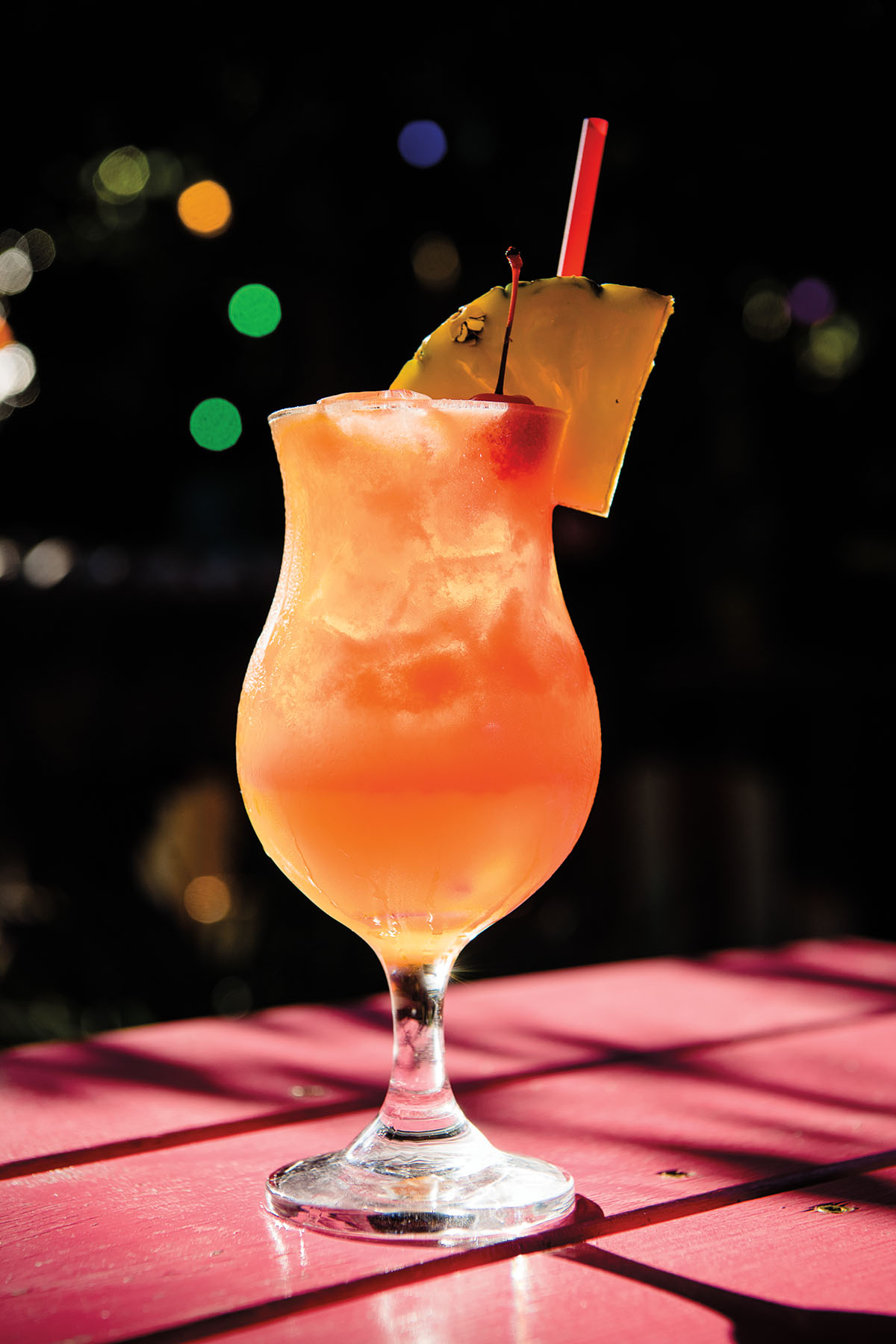 A glass of bright orangey-peach rum punch with a pineapple wedge on the side
