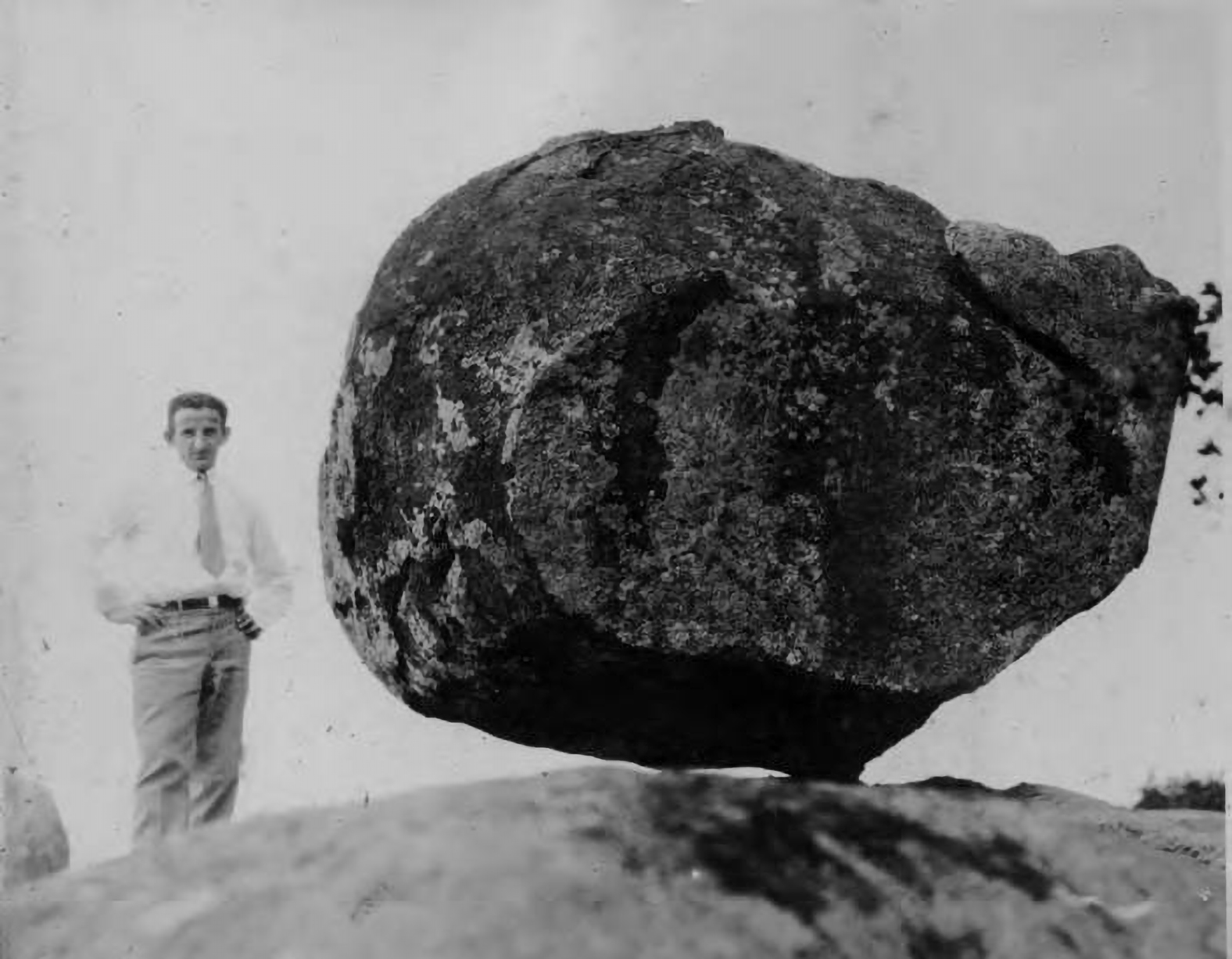 A man in a white shirt and tie stands next to a large dark gray boulder