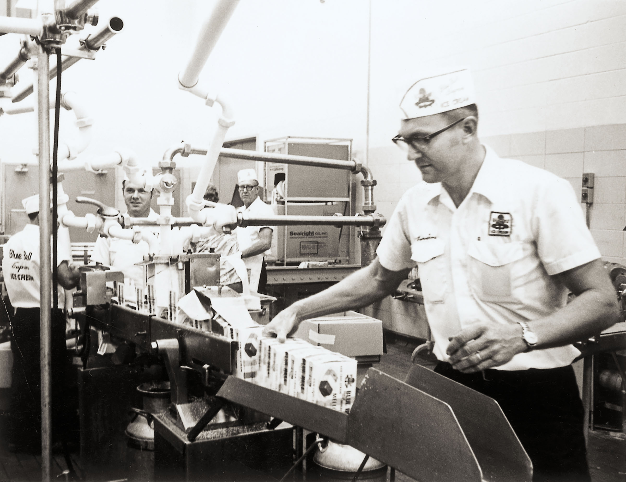 A historic photo of a man in a Blue Bell uniform and hat packaging ice cream
