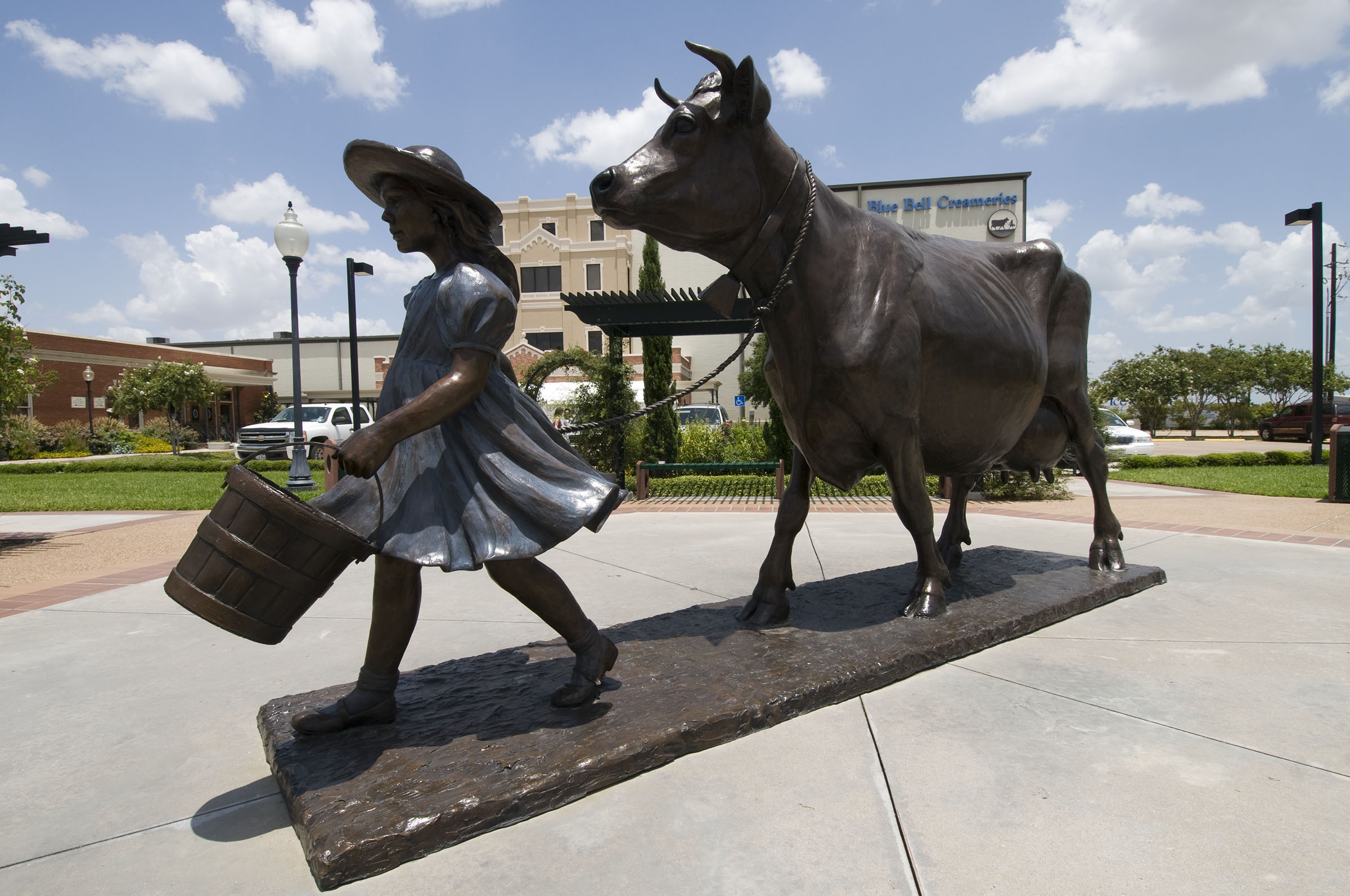 A statue of a girl leading a cow and holding a bucket under a blue sky