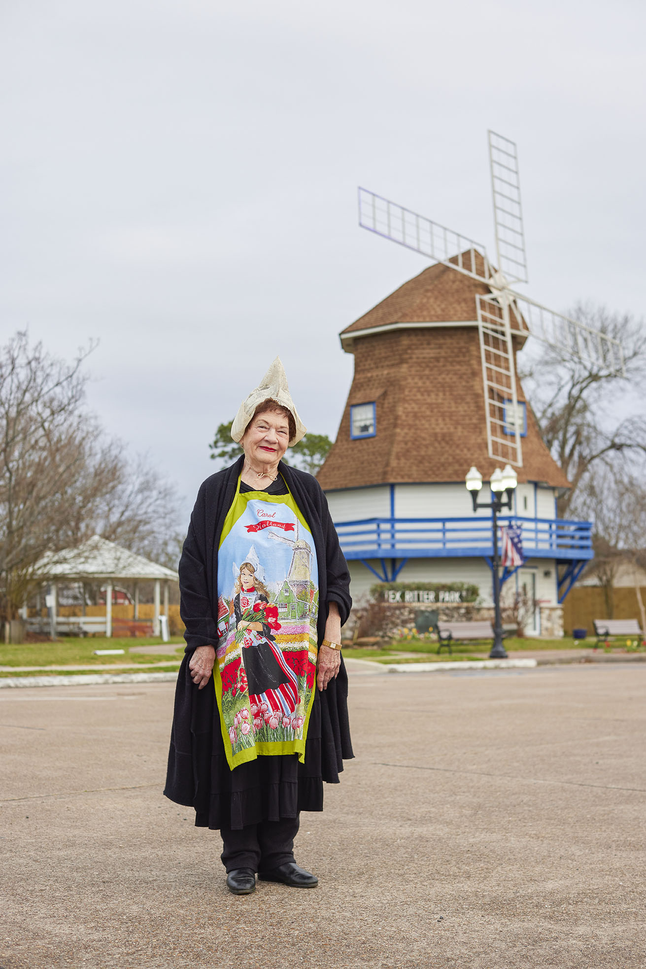 Curator of Dutch Windmill Museum stands in front of building in traditional bonnet.