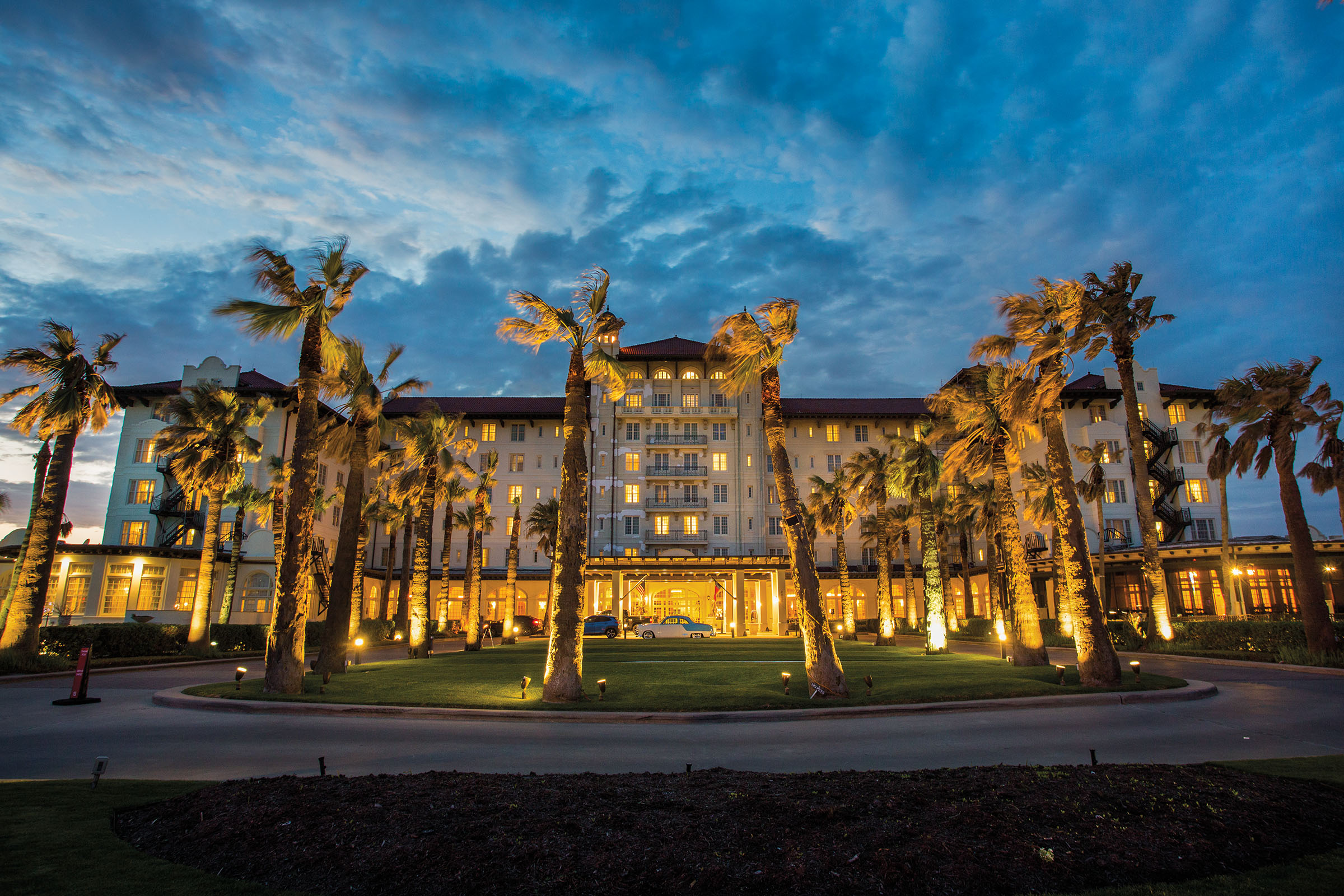 A hotel lit up at night with tall palm trees in front