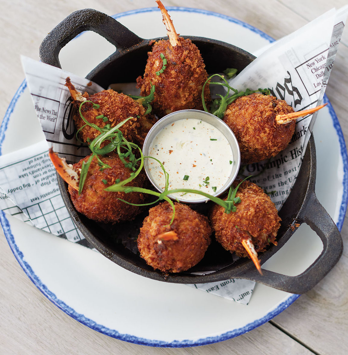 An overhead view of golden-fried pieces of crab in a cast-iron dish with dipping sauce