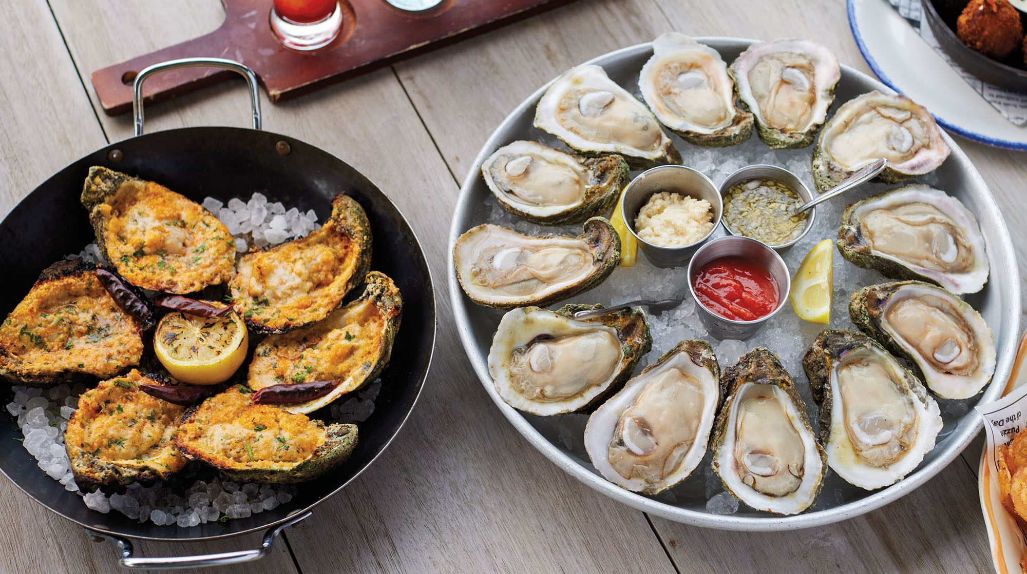 An overhead view of two platters of oysters -- on the left, cooked golden brown oysters and on the right, a plate of raw oysters on the half-shell with traditional cocktail sauces