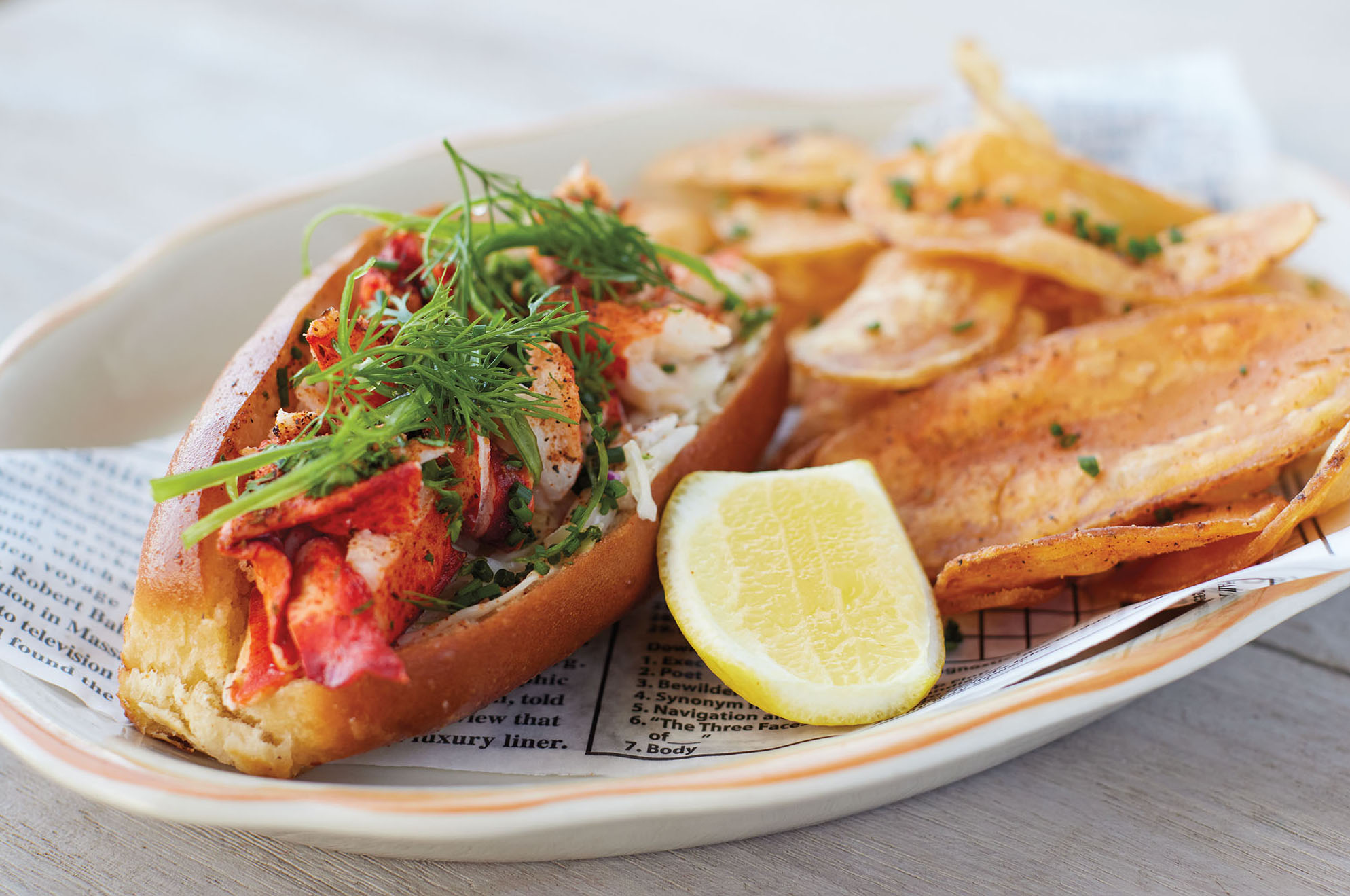 A lobster roll paired with a lemon and fries sits on a plate