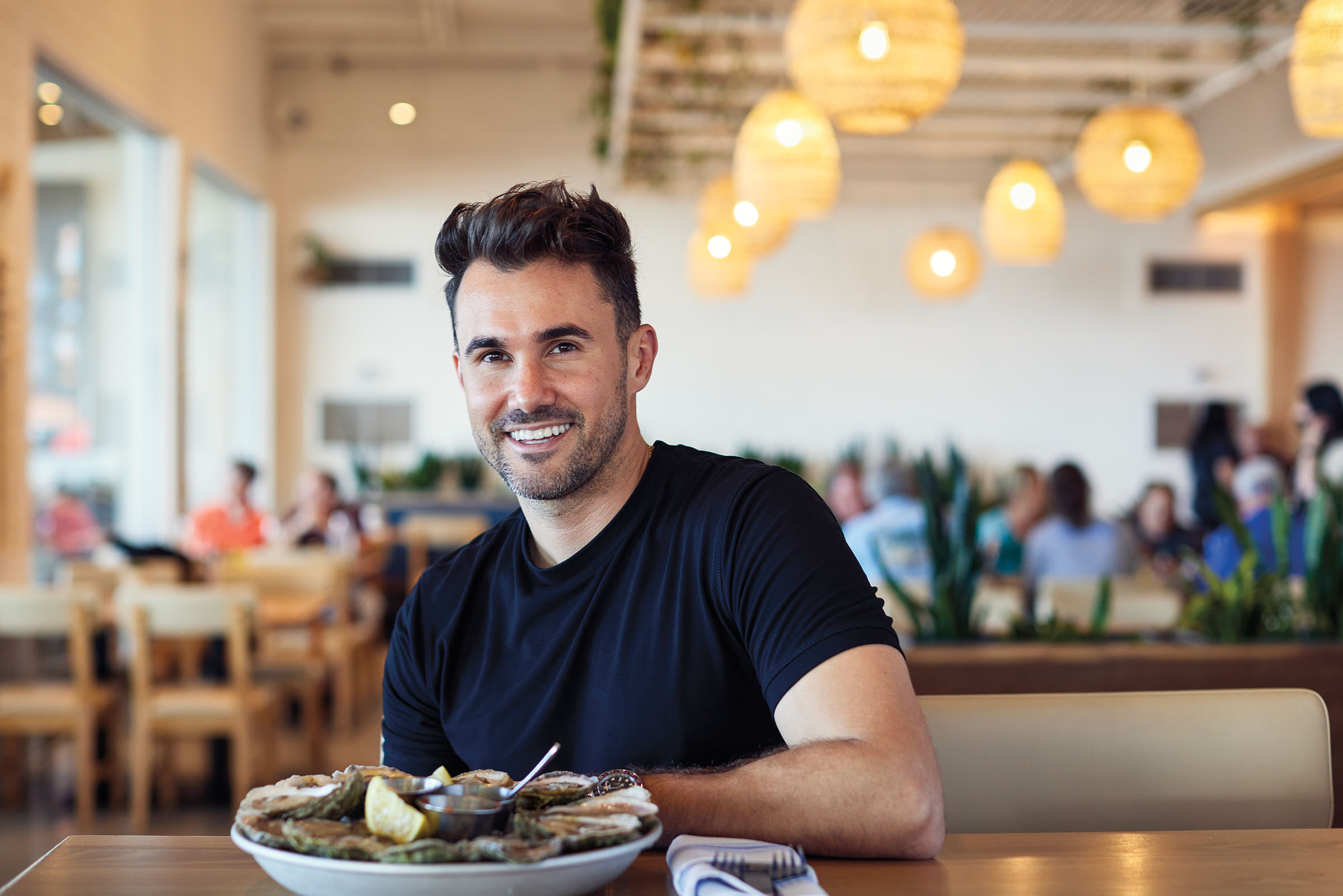 A man in a black shirt sits in a restaurant behind a plate of oysters