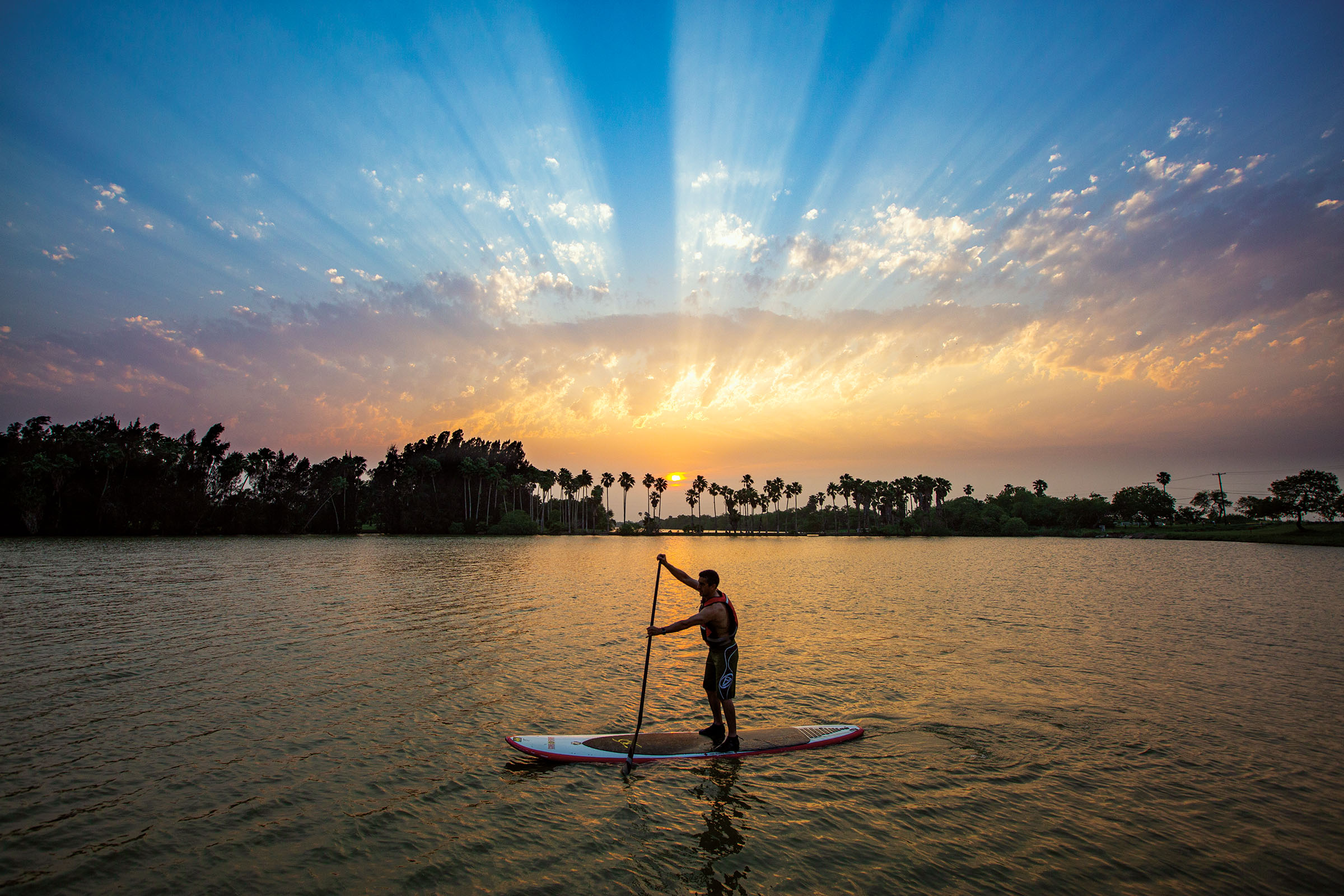 A sihlouette of a person on a paddleboard in front of a beautiful blue and gold sunset