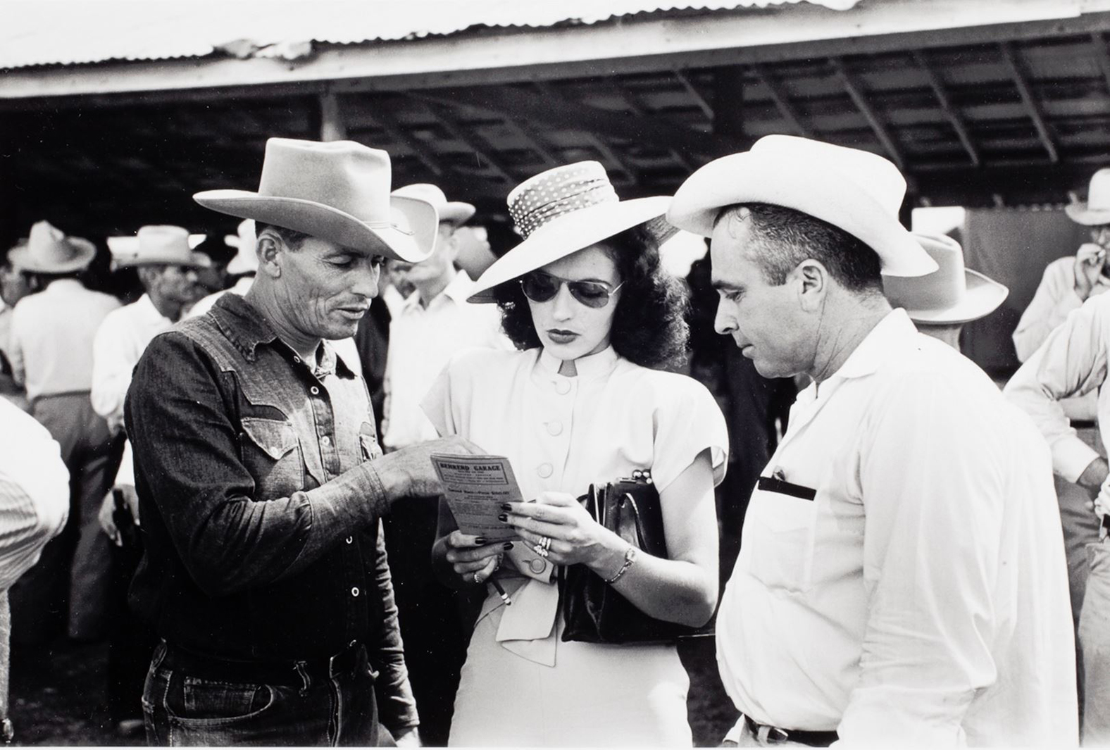 Three people in hats point to a small schedule in a woman's hand