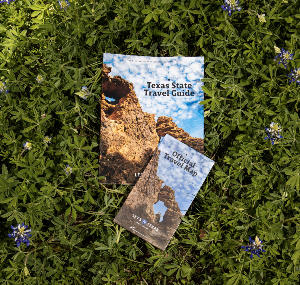 An overhead view of a map and travel guide on green grass and bluebonnets