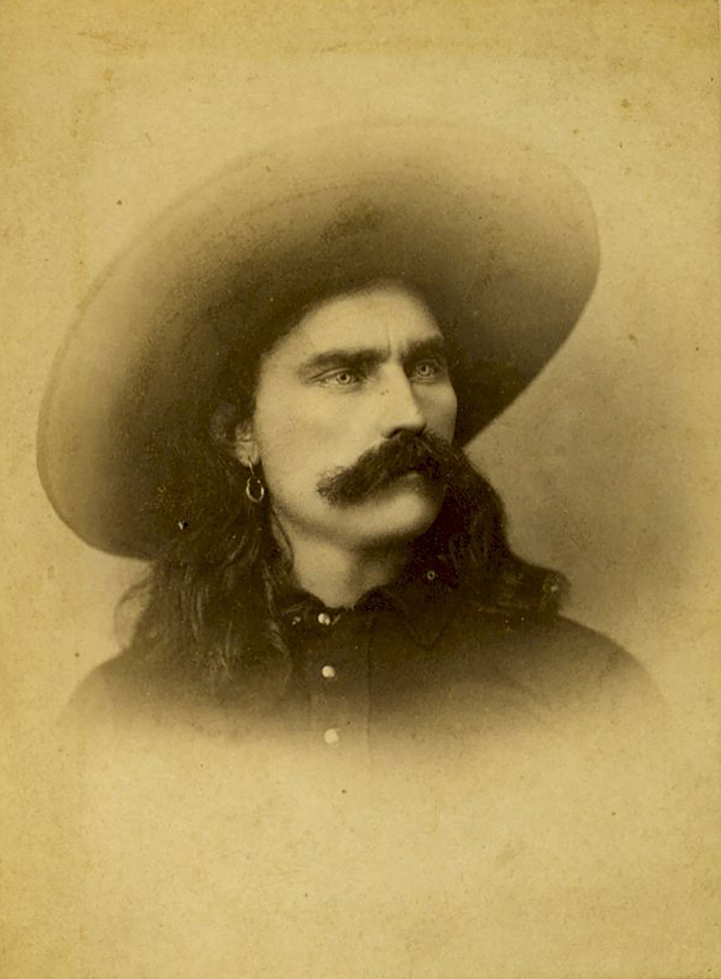 A yellowing historic photo of a man with a mustache in a large hat