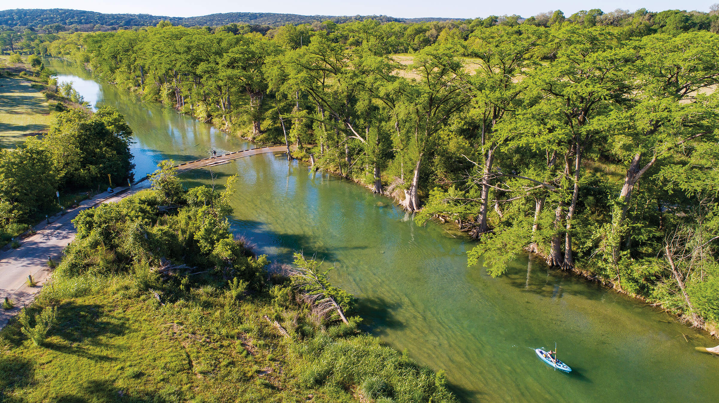 An overhead view of the wide blue Blanco river with boats in the middle and trees on the side