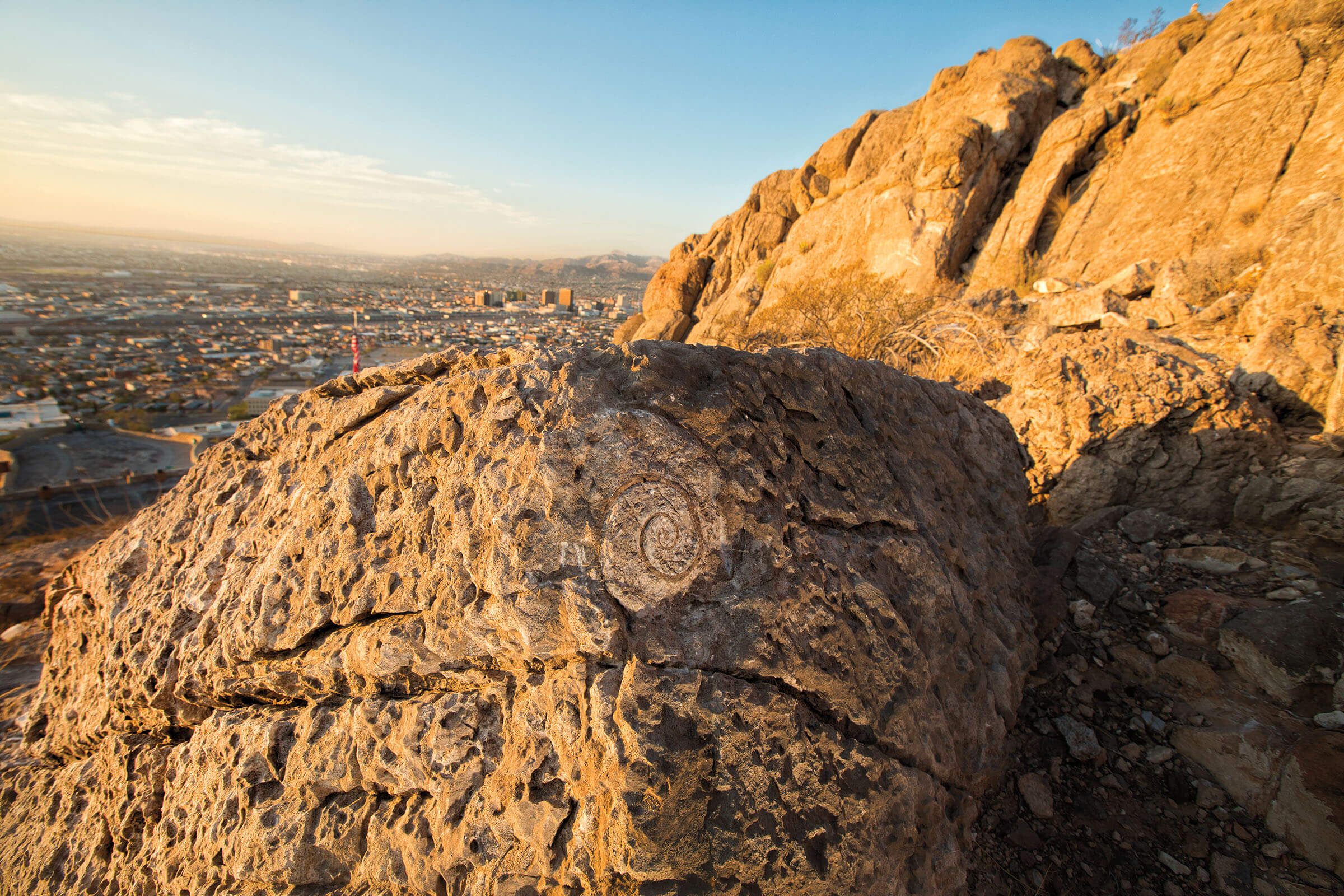 The sun sets over desert rock with fossils visible in front of a wide blue sky