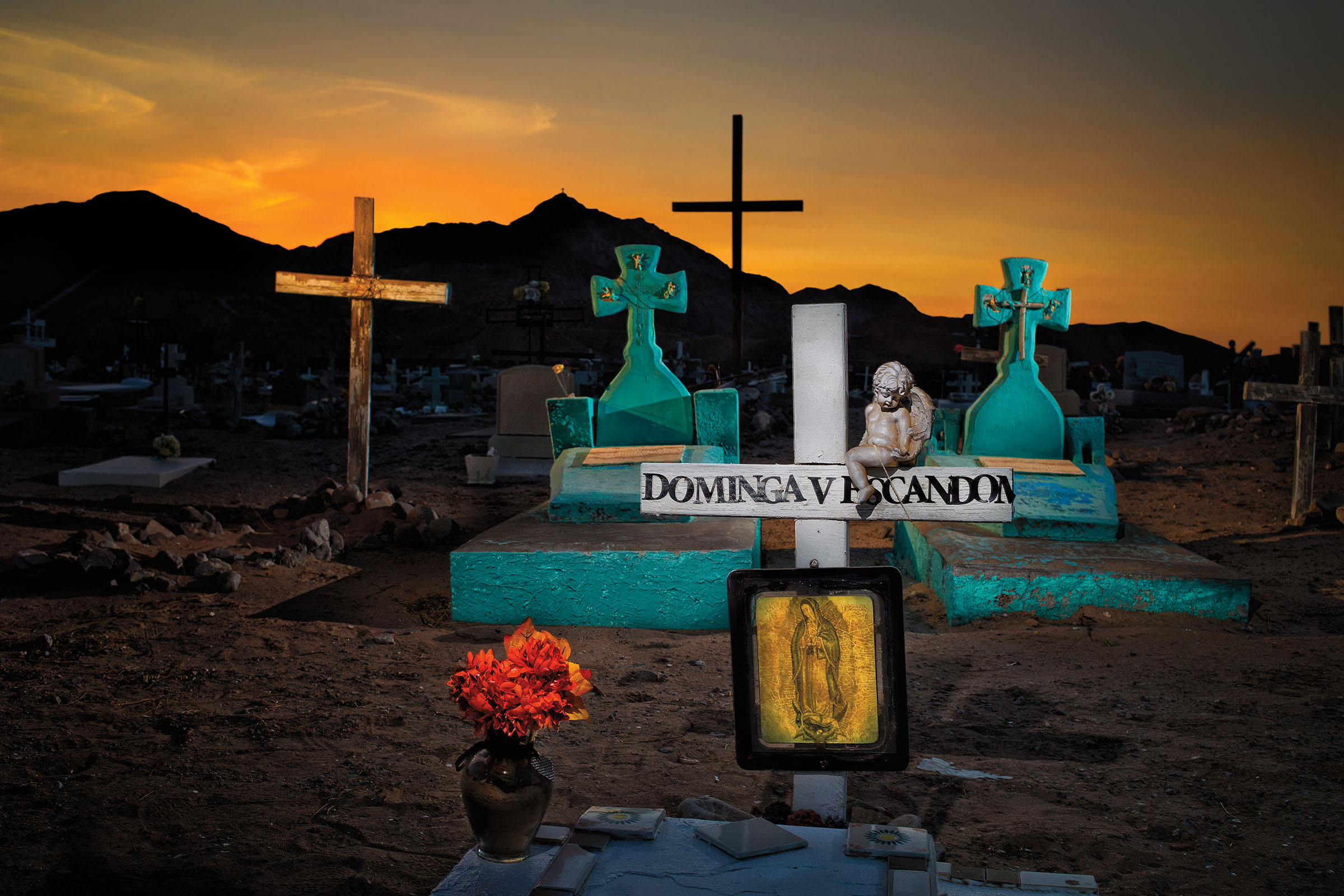 Bright turquoise and gold and white headstones in a cemetery in front of a yellow sunset