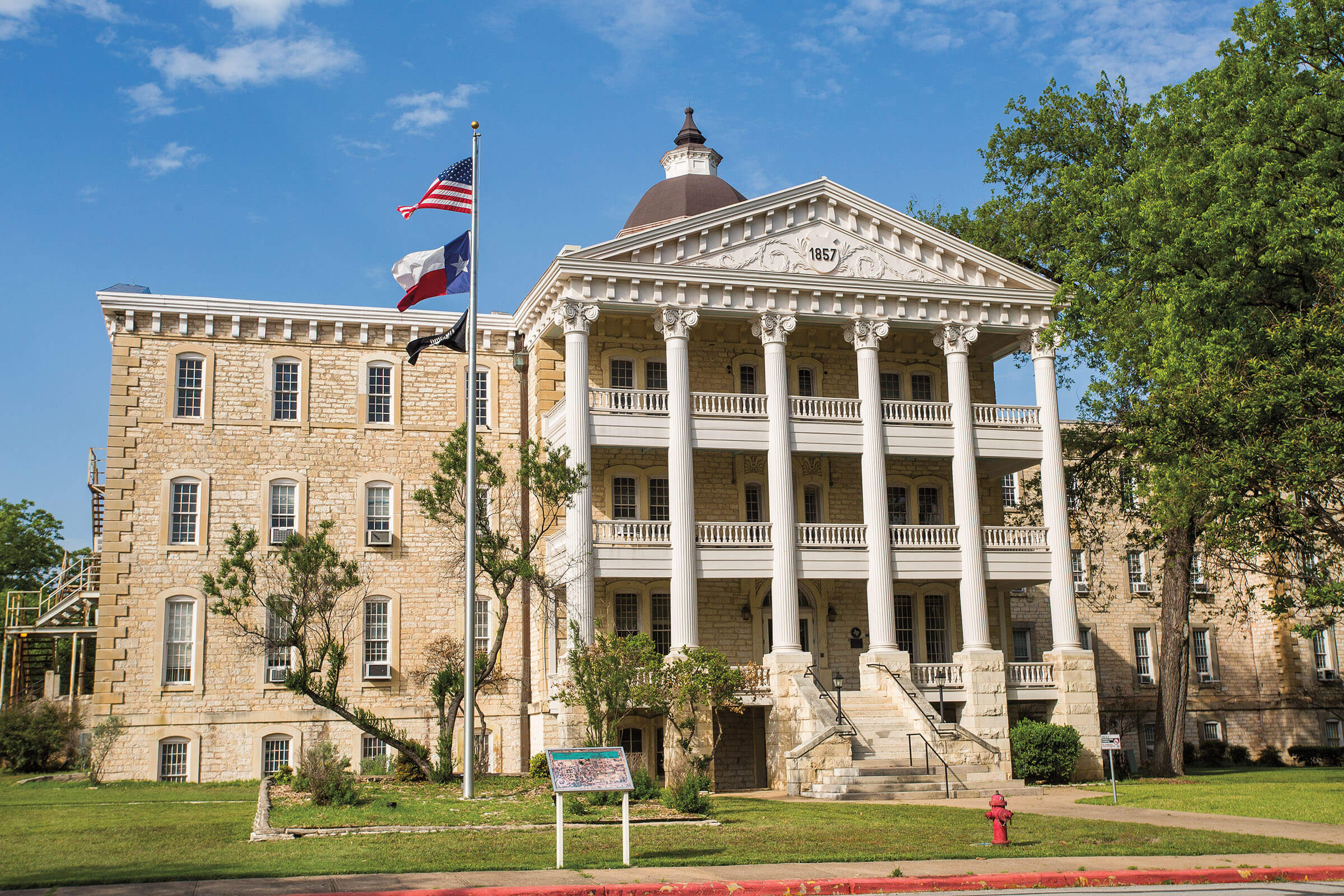 The outside of a three-story stone building with a Texas and United States flag flying
