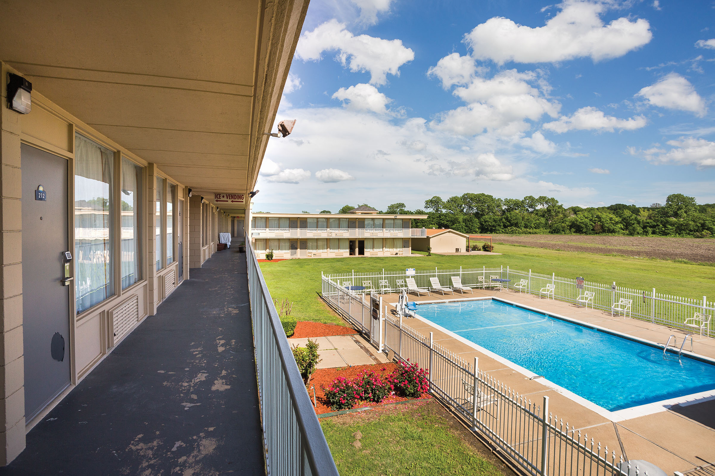 The view down an ourdoor breezeway of a model above a glittering blue pool under blue cloudy skies