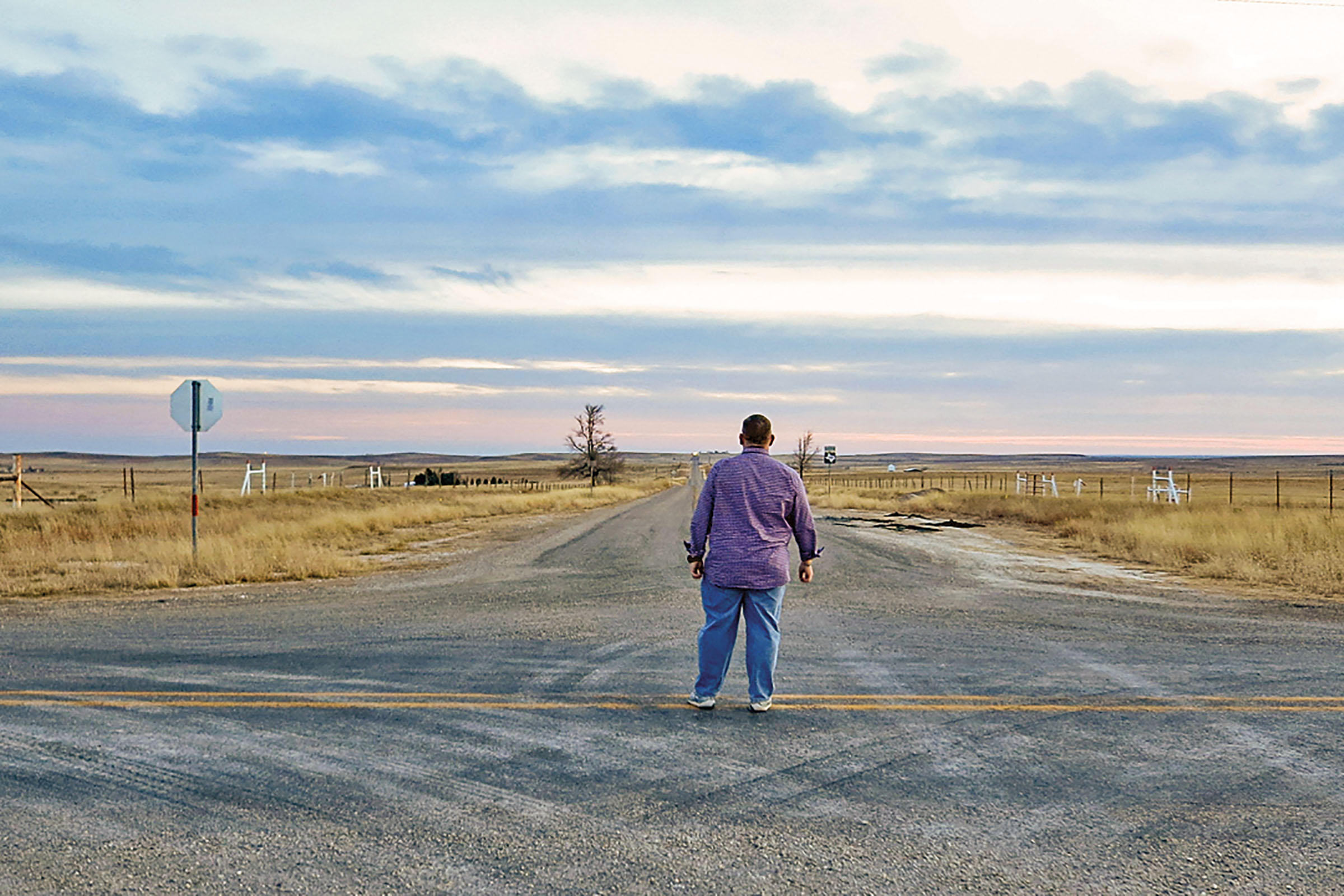 A man in a purple shirt looks down a field next to a stop sign