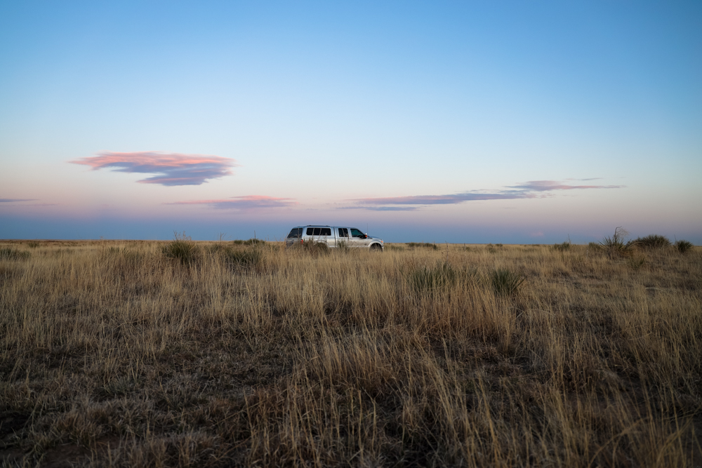 A truck parks in a wide grassy field underneath a blue and pink sky