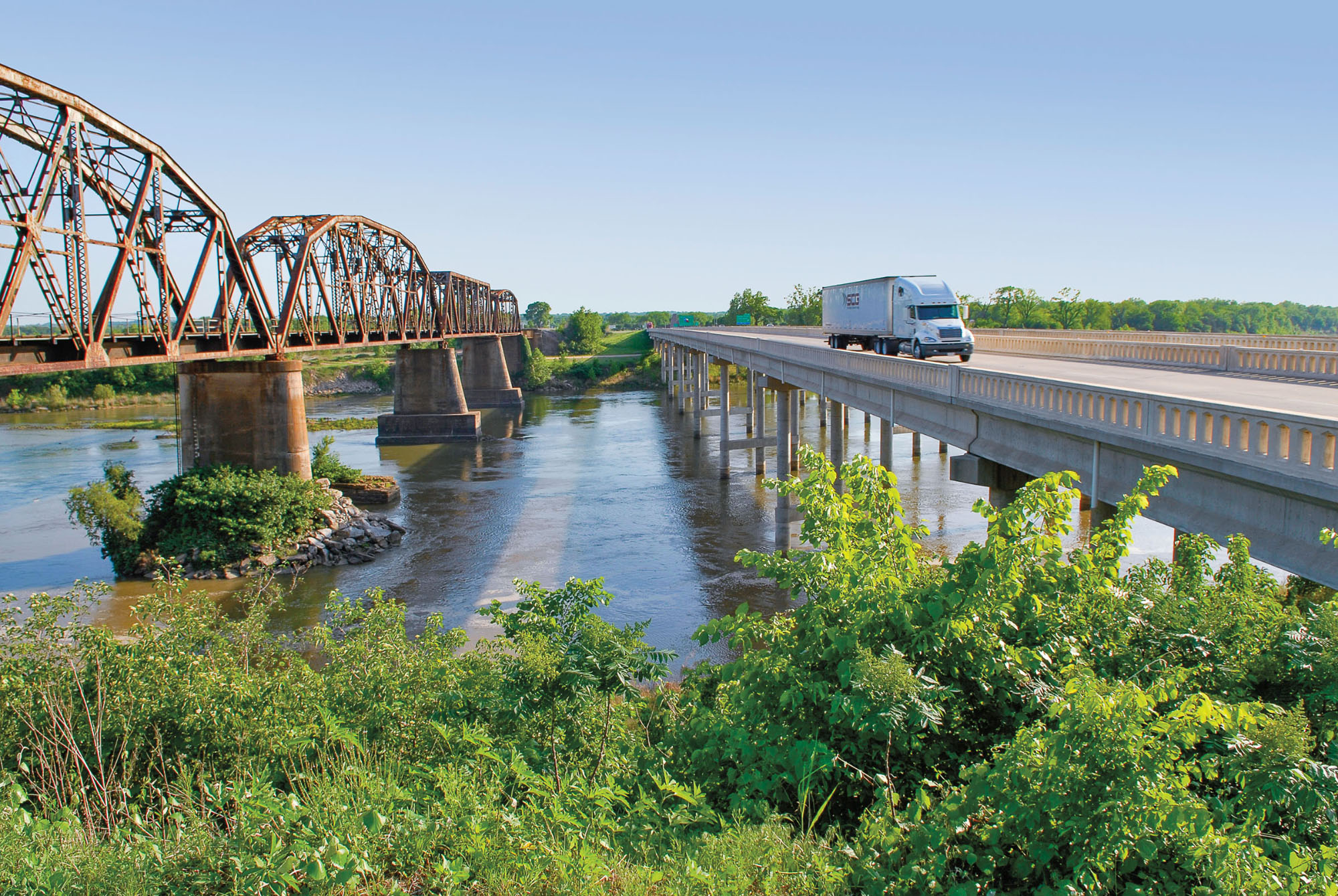 Trucks cross two bridges over water and trees