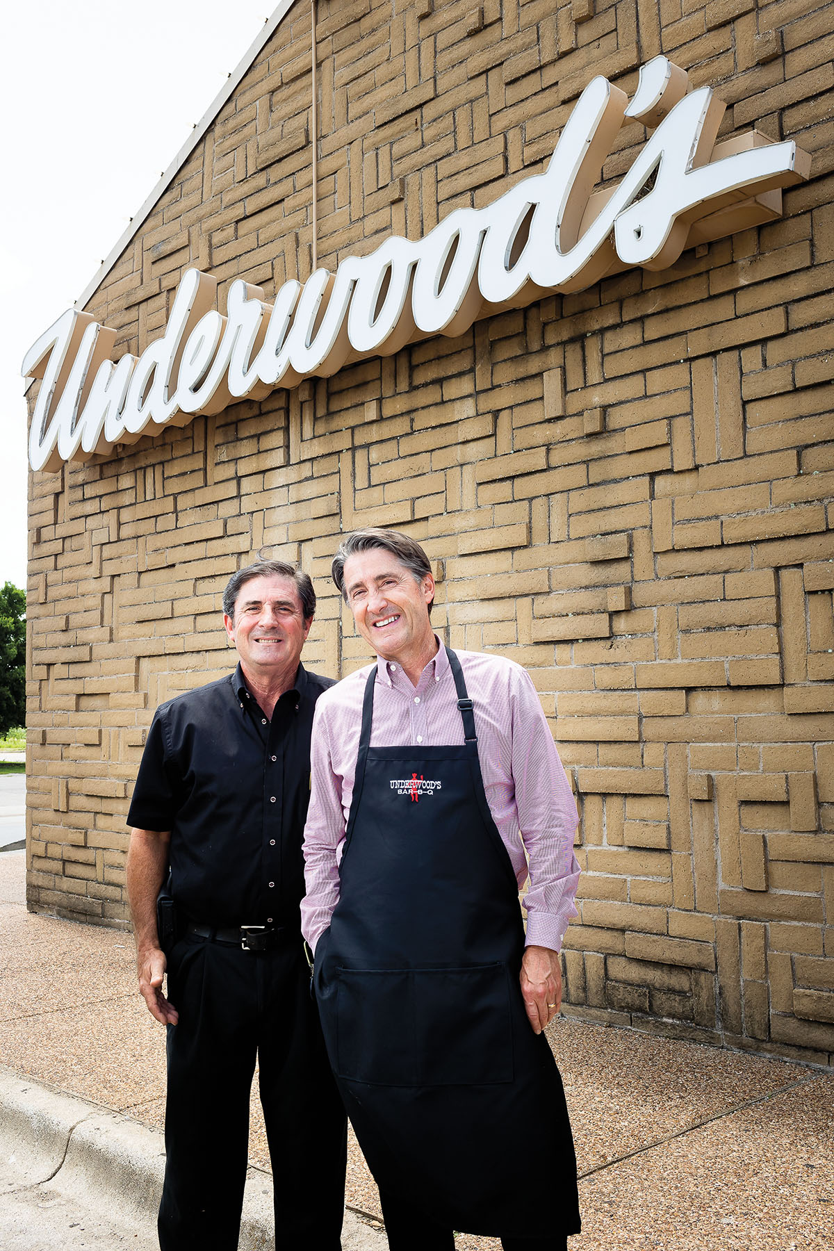 Two men, one in an apron, stand out front of a building with a sign reading "Underwood's"