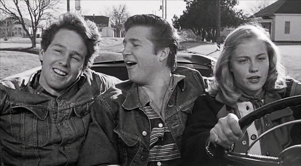 A black and white screen capture of a group of young people in a car