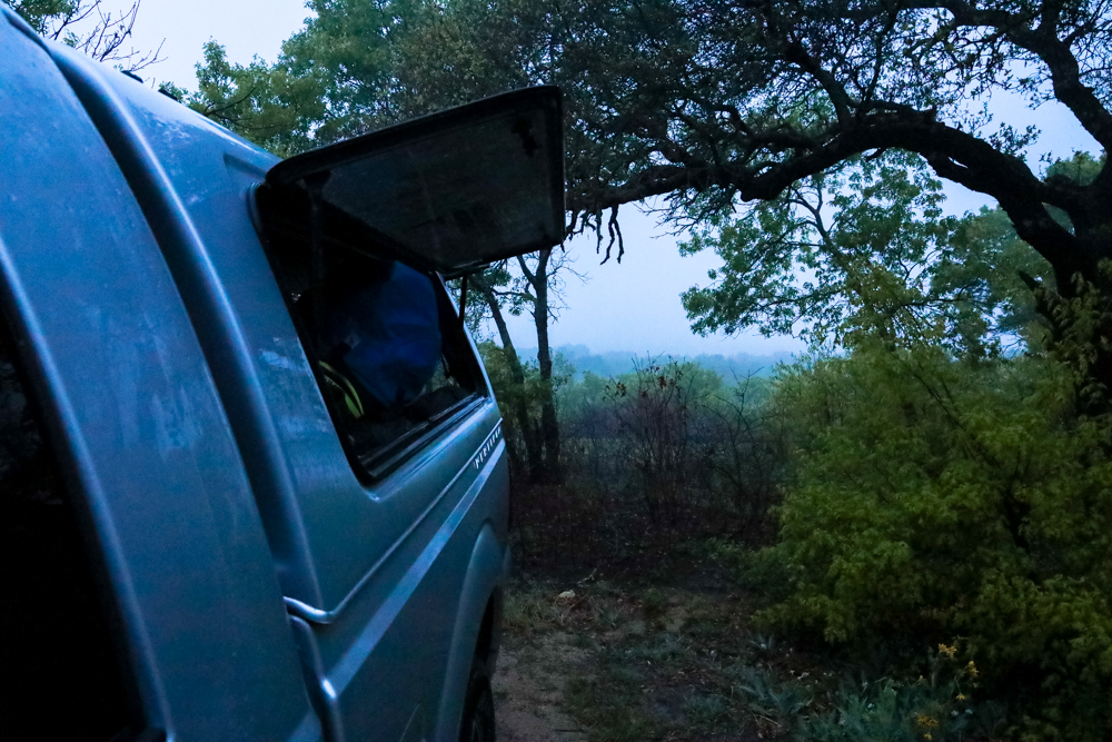 A truck parked near water under green trees with the topper opened