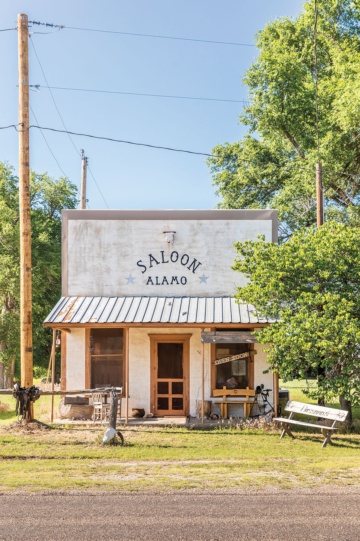 A white painted building next to a telephone pole with a sign reading "Saloon Alamo"