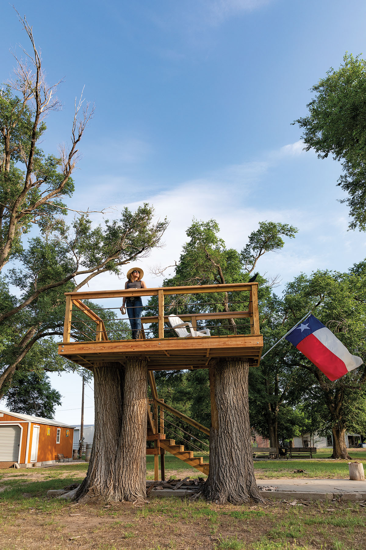 A man stands on a platform in the trees next to a Texas flag