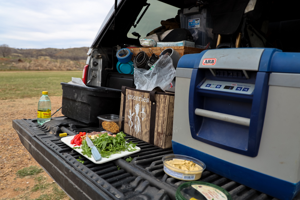 A lunch of vegetables, crackers, hummus and Topo Chico on the tailgate