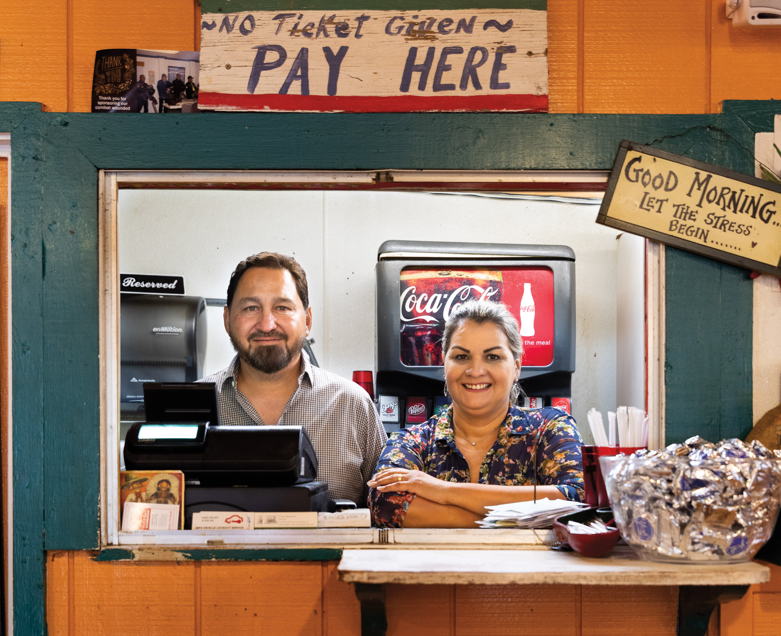 A man and woman stand behind a restaurant counter under a sign that says "No ticket given, pay here"