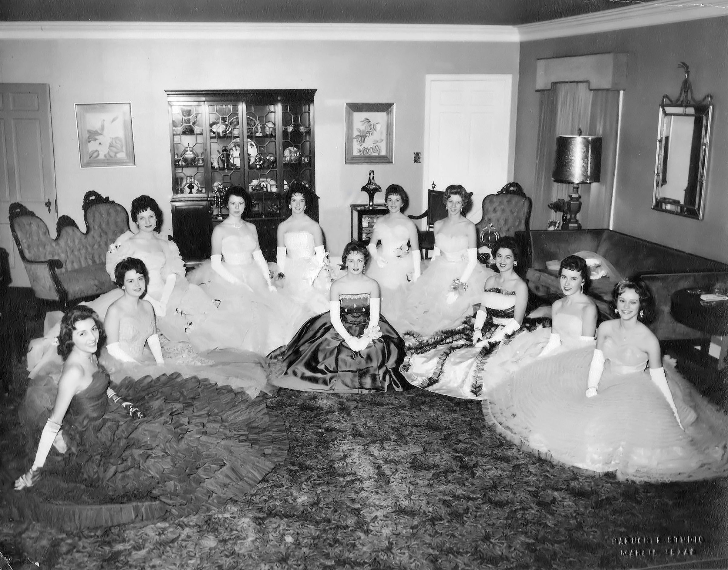 Eleven women in elegant dresses pose for photo in living room