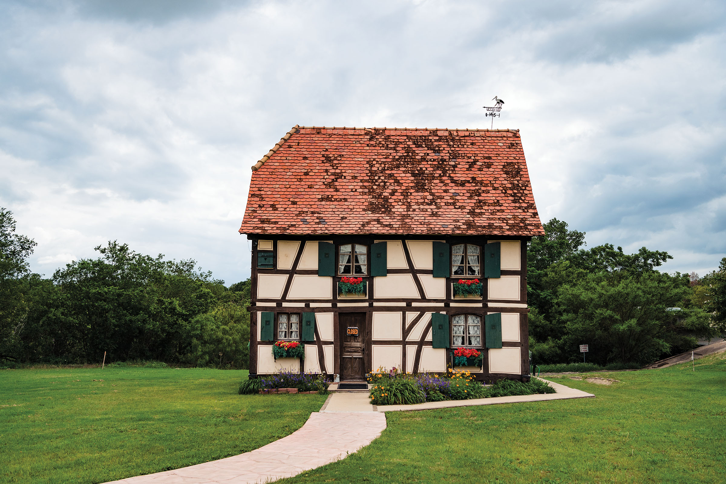 A European-style cottage on bright green grass in front of dark green trees