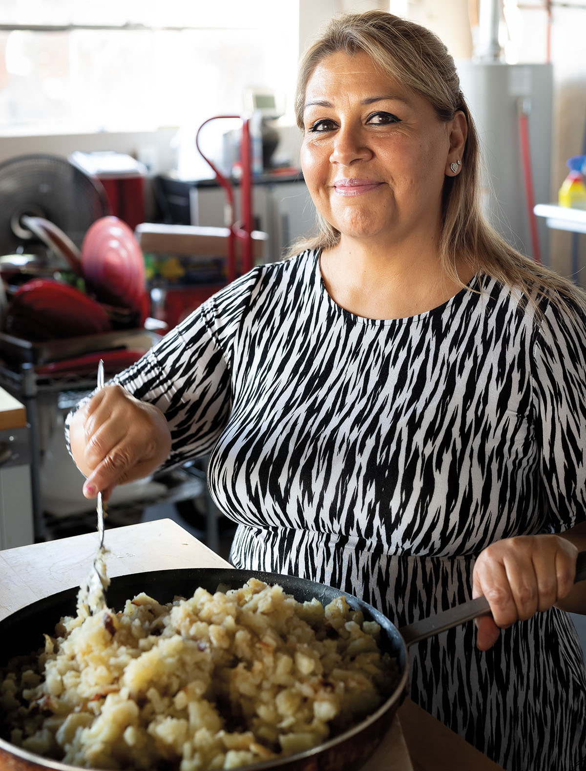 A woman in a black and white striped shirt stirs a large portion of food