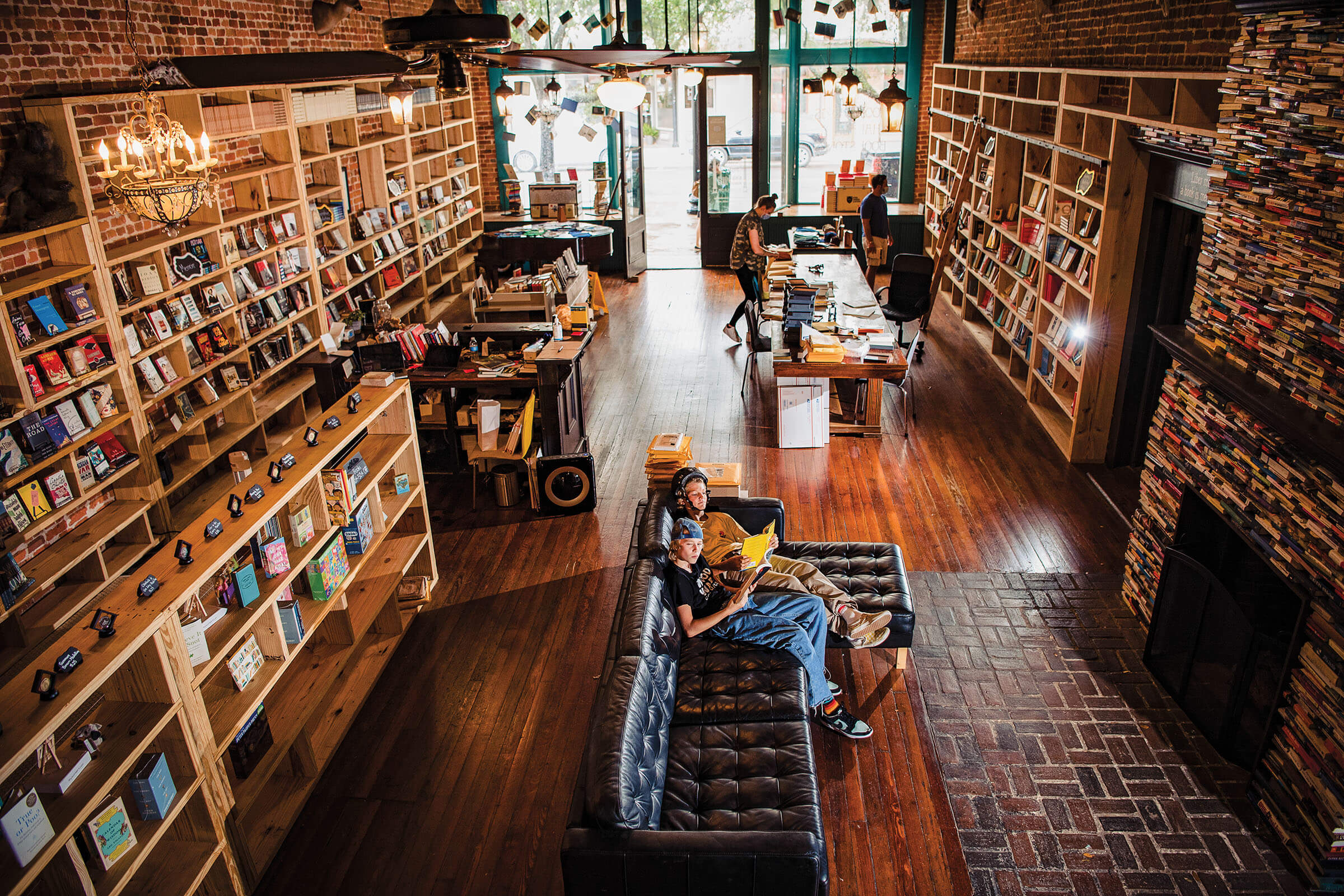 People sit on a large leather couch surrounded by books in a wood-paneled and brick bookstore
