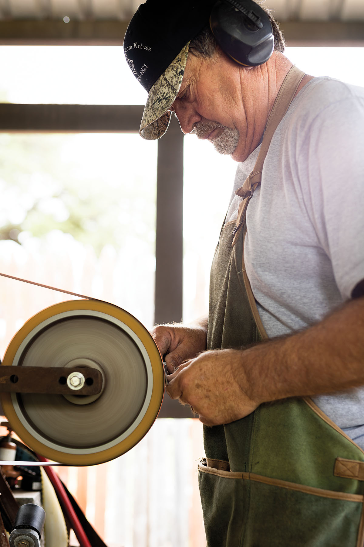 A man in an apron wearing ear protection works on a sharpening stone