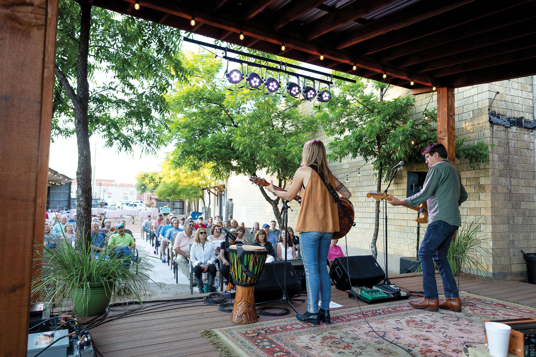 A man and woman perform on a stage to a small crowd outdoors