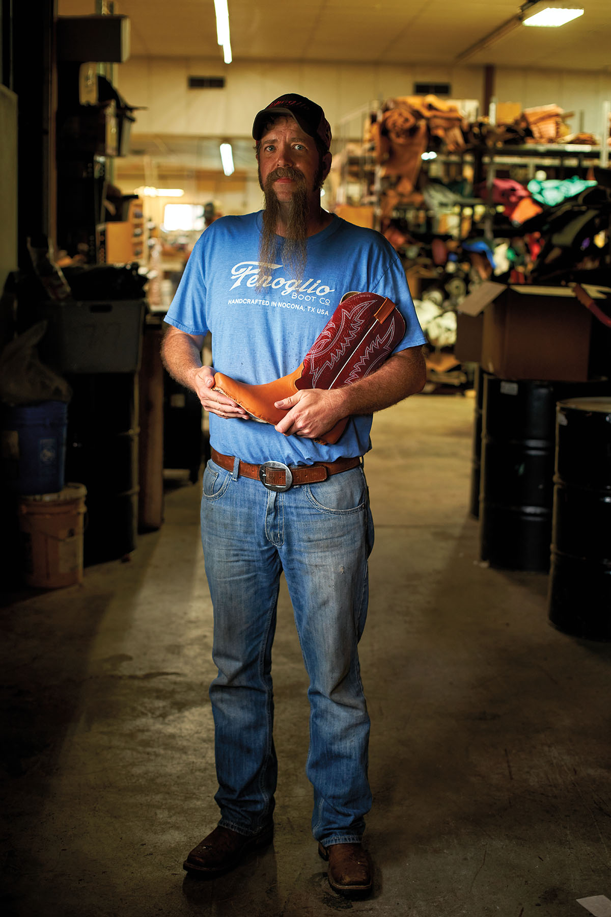 A man in a blue shirt and jeans holds a cowboy boot in a store