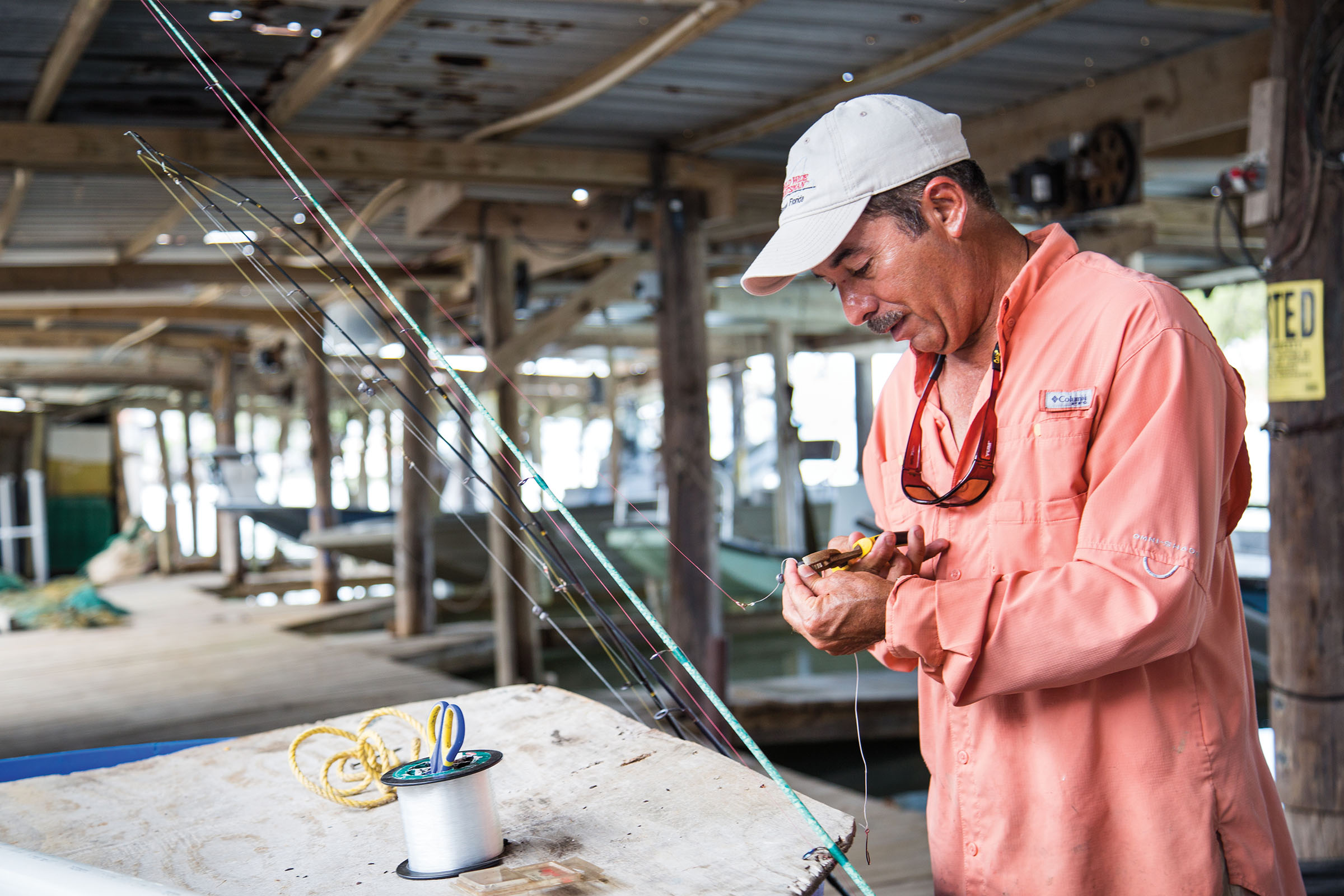 A man in a white hat and salmon-colored shirt works on a fishing rod