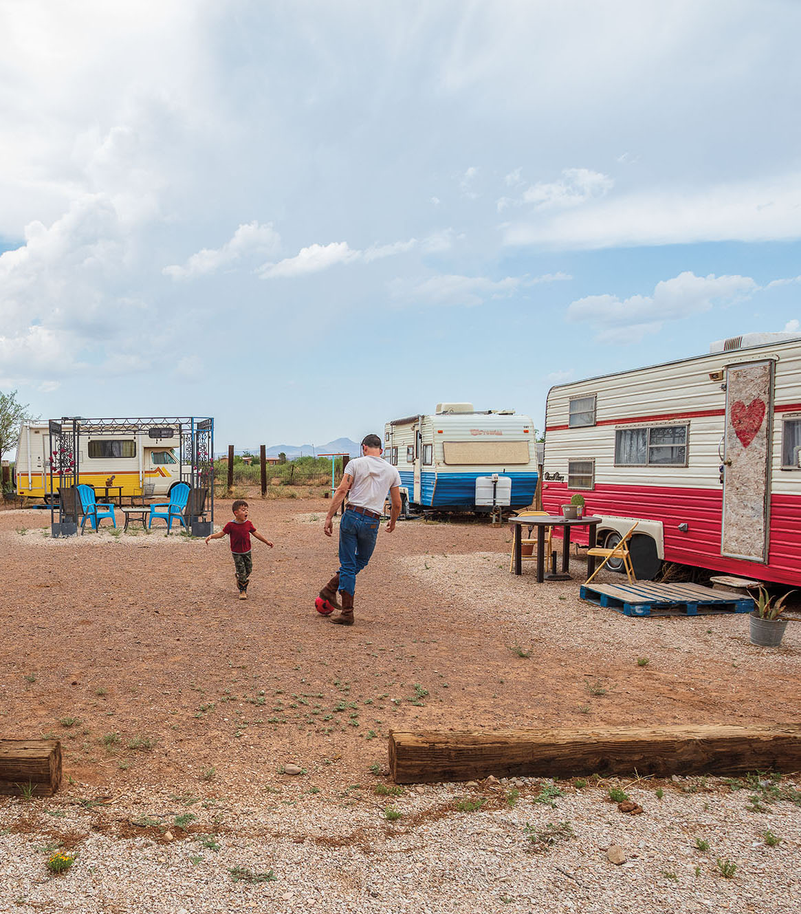 A man and a young man kick a ball surrounded by colorful RV trailers