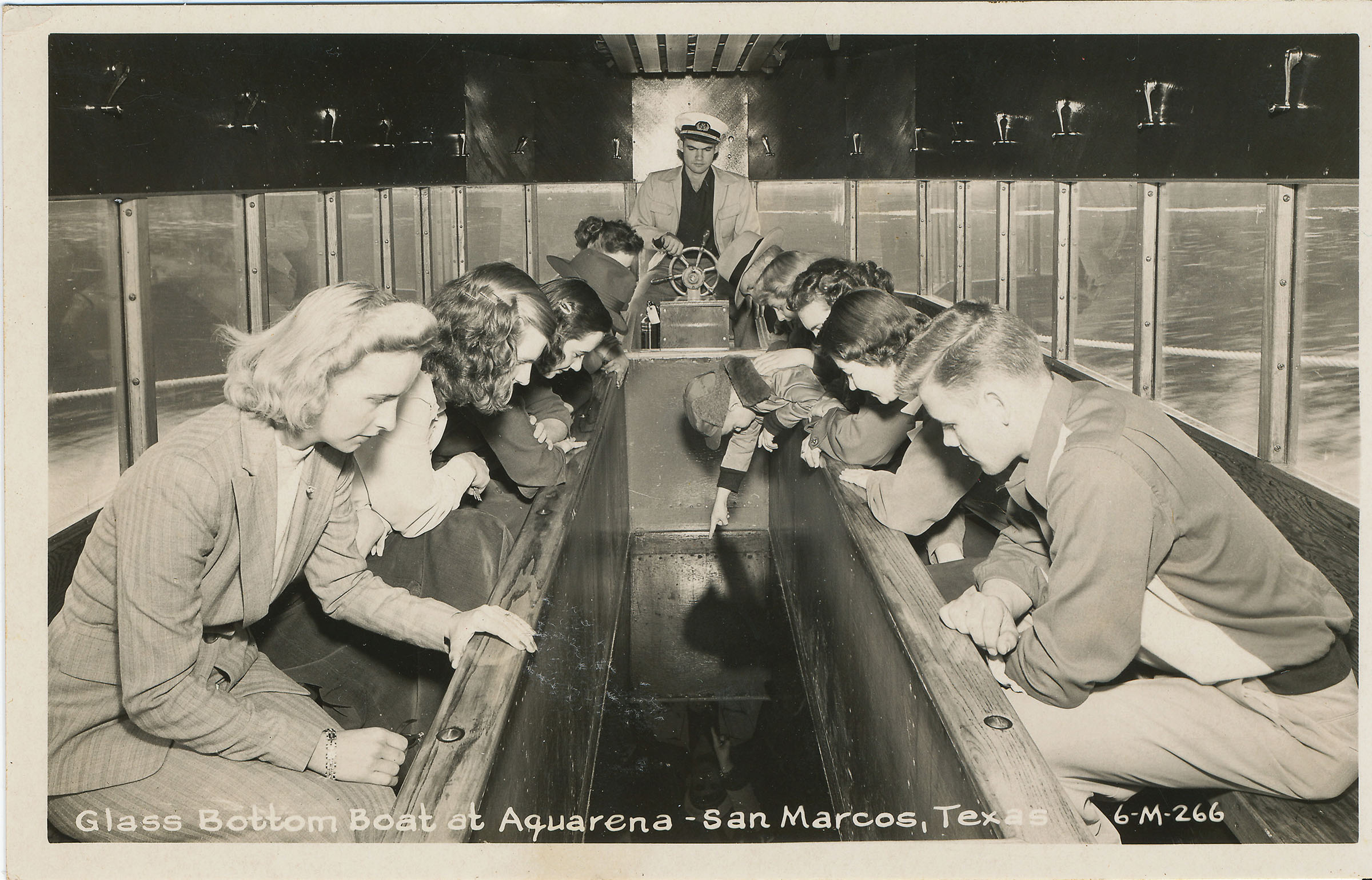 A group of people look through the bottom of a glass-bottomed boat in a vintage photograph