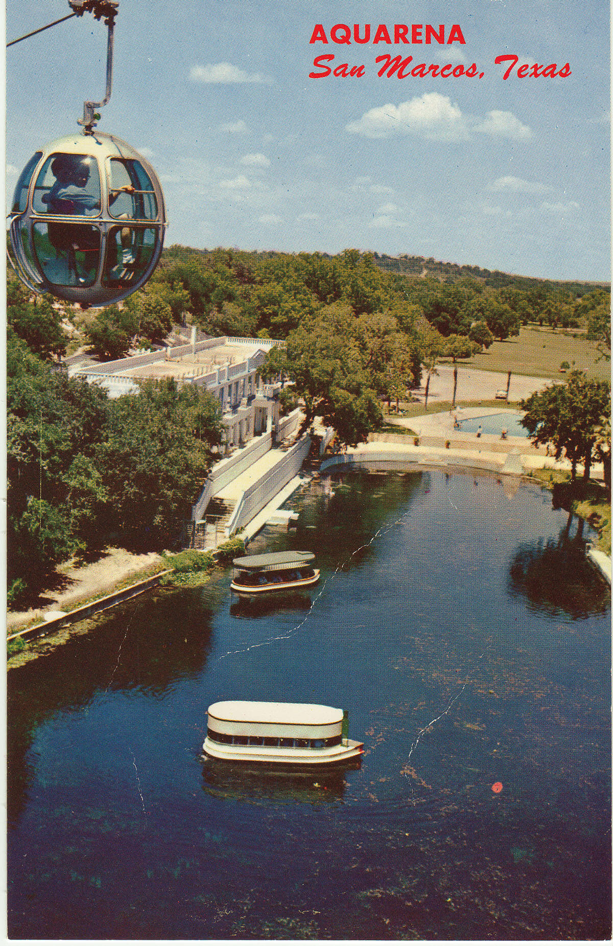 A bright blue postcard showing an overhead view of Aquarena Springs and a sky ride