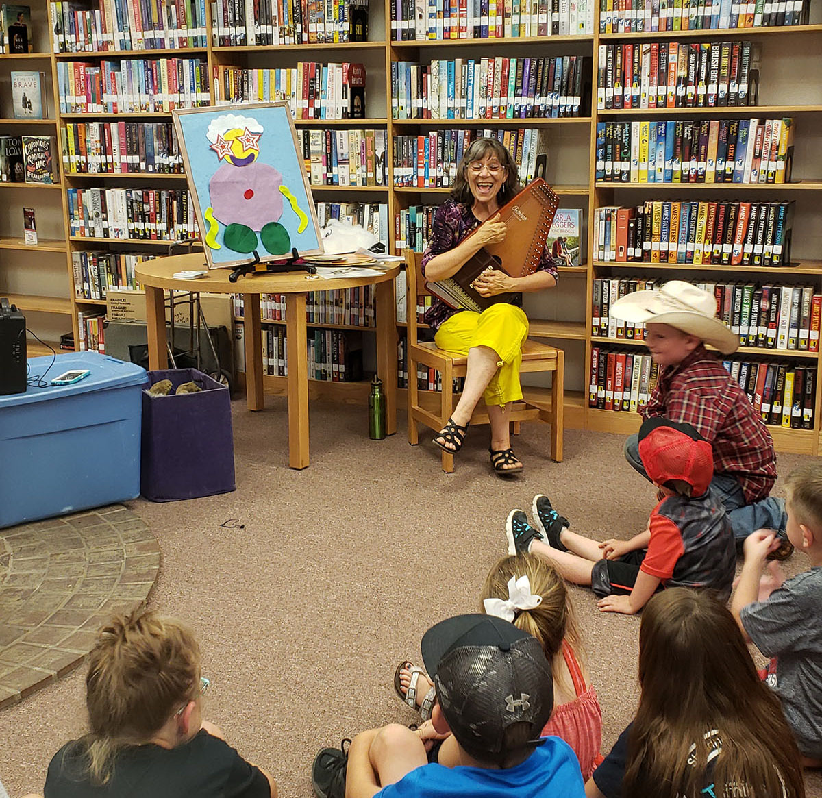 A woman plays an instrument in a library surrounded by children