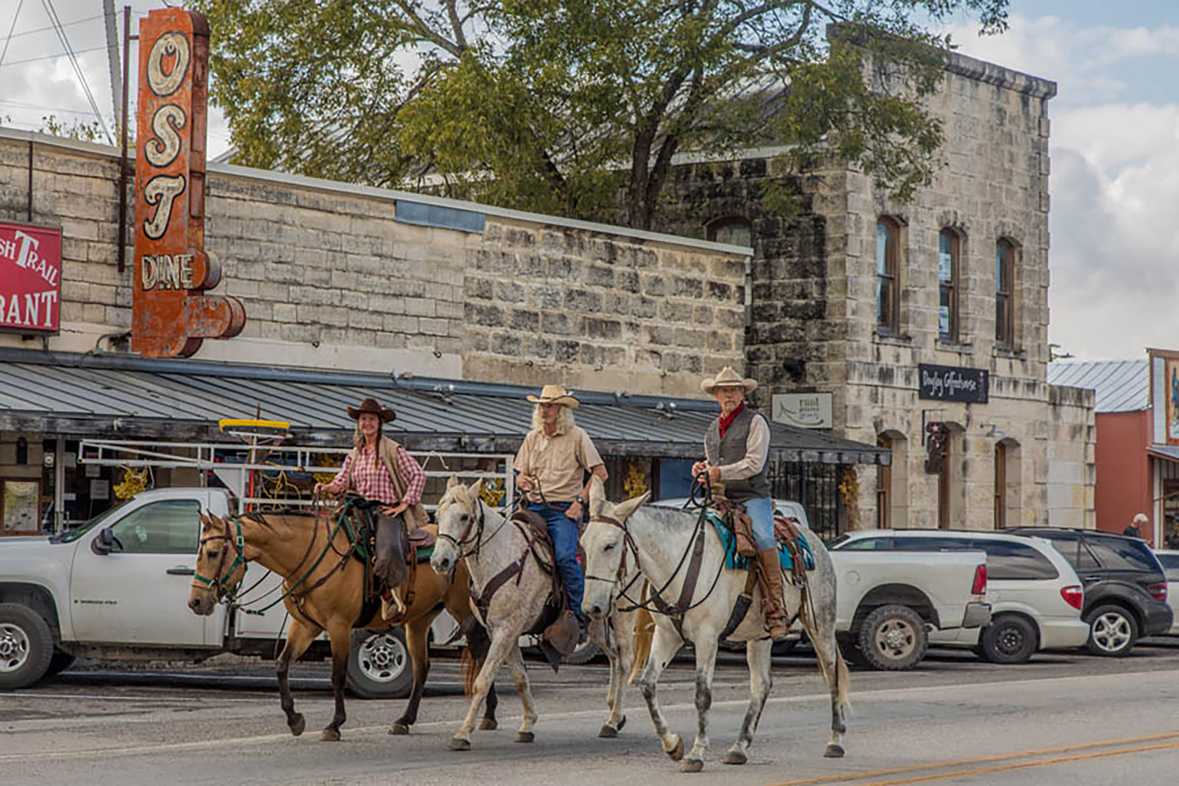 Three people on horses ride through town of Bandera