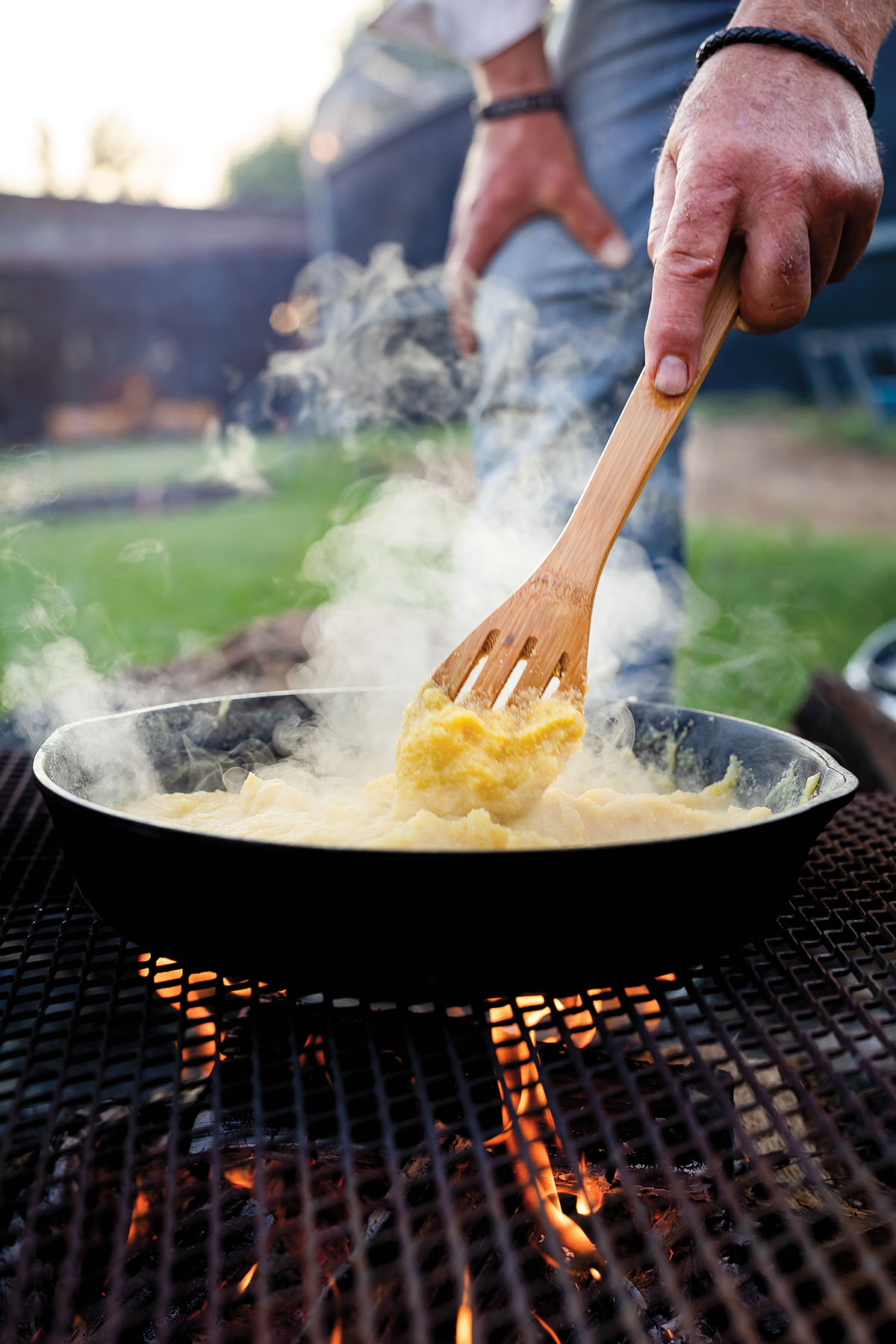 A woden spoon stirs steaming corn inside a cast iron skillet