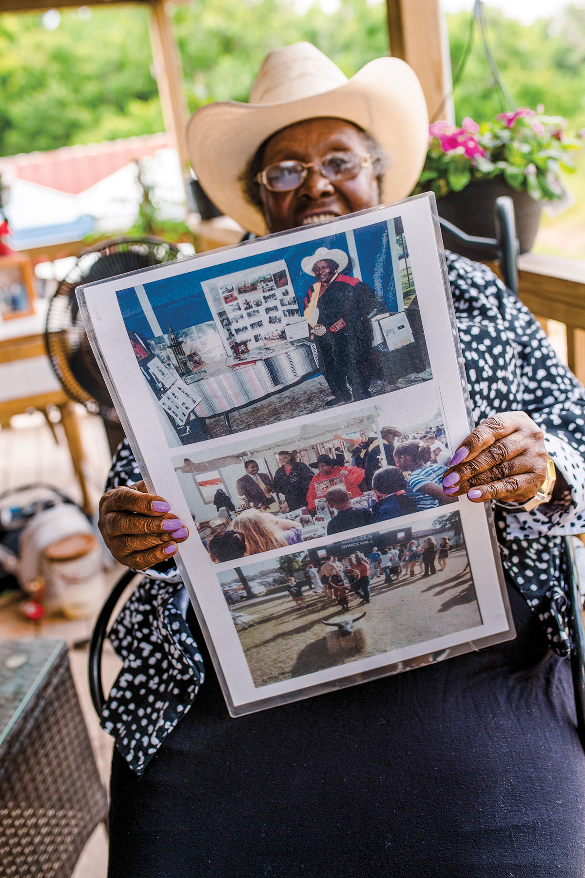 A woman in a cowboy hat sits holding up laminated photographs of her