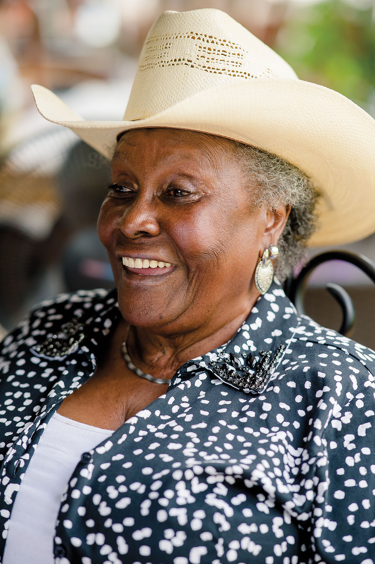 A woman in a tan cowboy hat and pattern shirt smiles