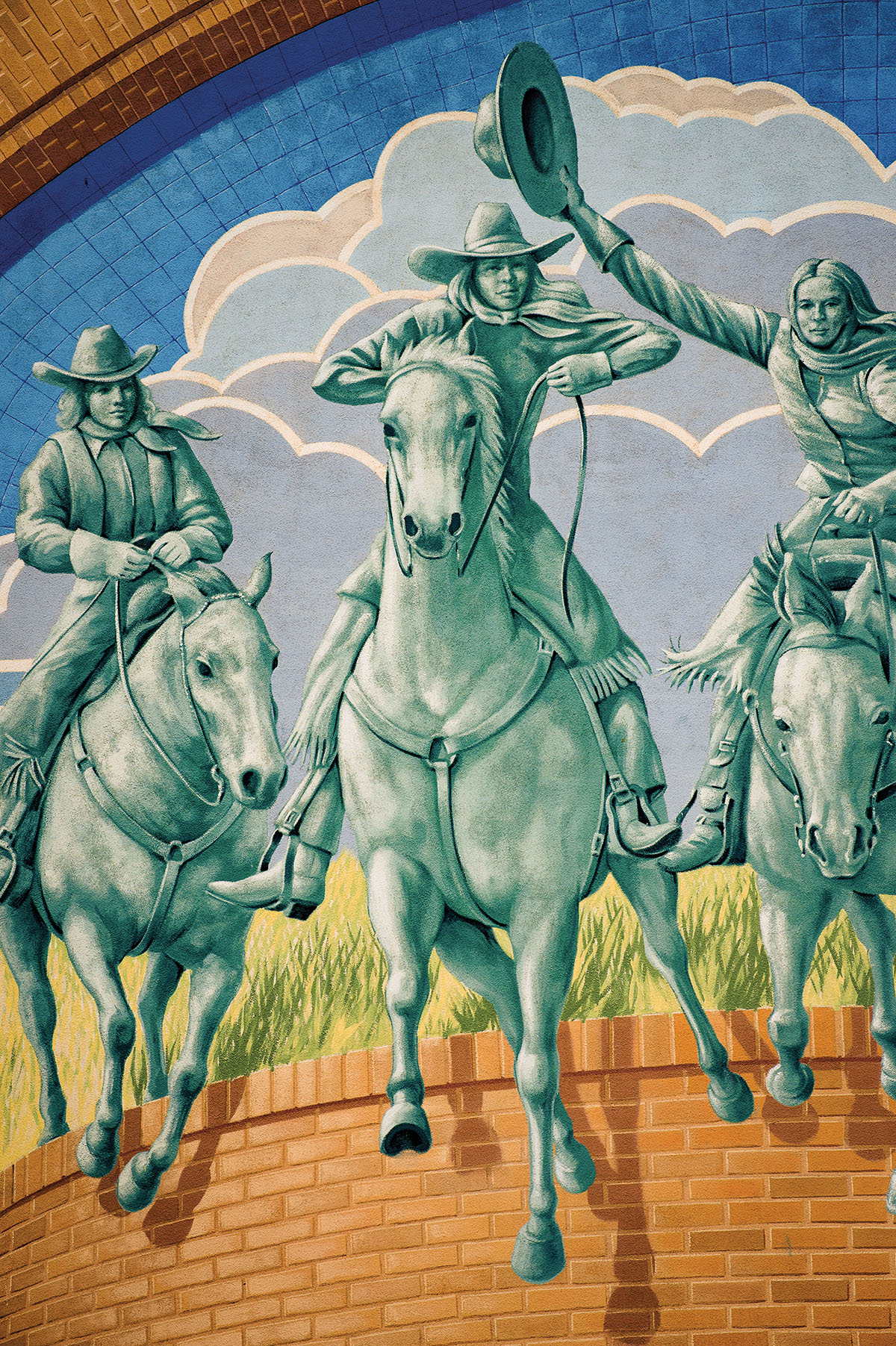 A mural of green-tinted cowgirls riding horses with blue clouds in the background