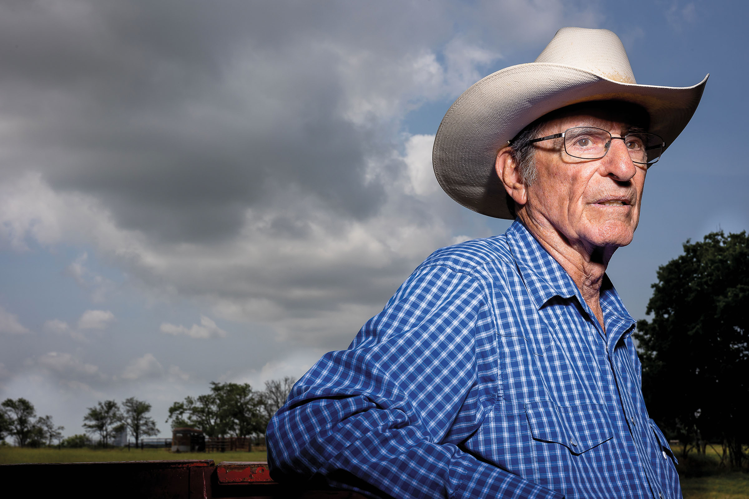 A man in a blue checkered shirt and light gray hat looks off into the distance under cloudy skies