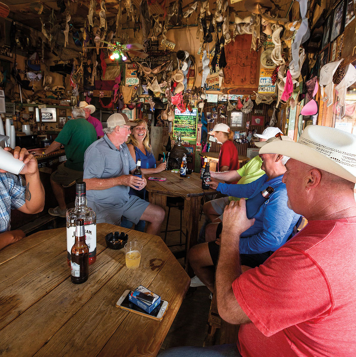 A group of people sit having drinks in a crowded, wood-paneled bar