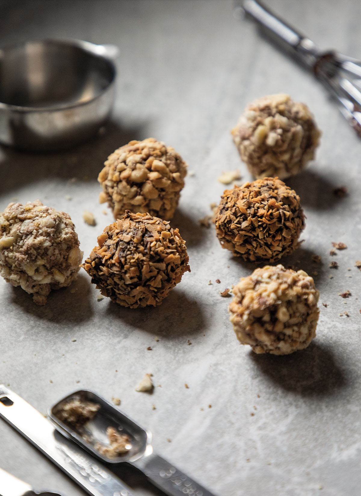 A group of small chocolate-brown truffles with nut topping on a slate top