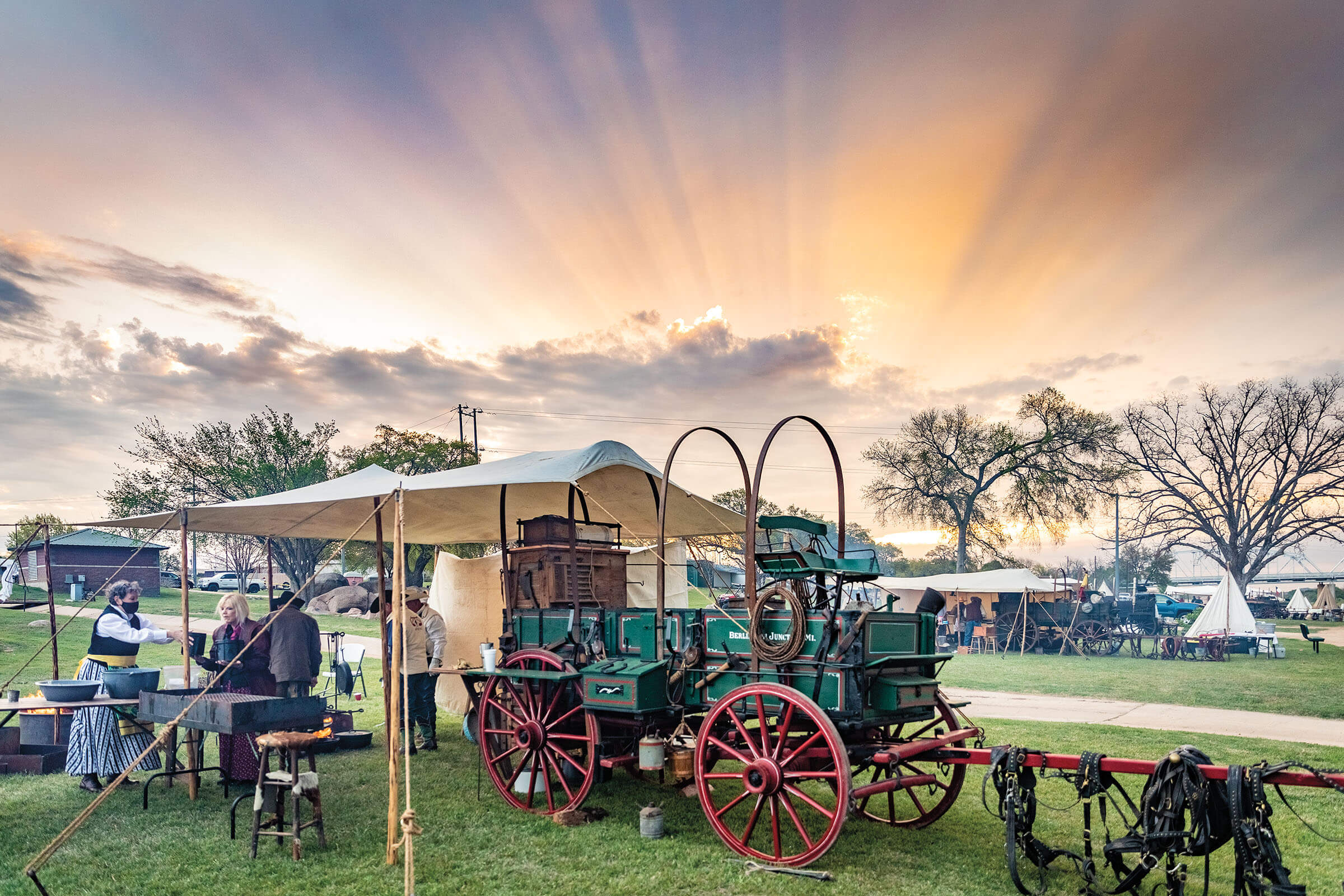 A golden sunrise behind a blue-green chuckwagon with a few people in front